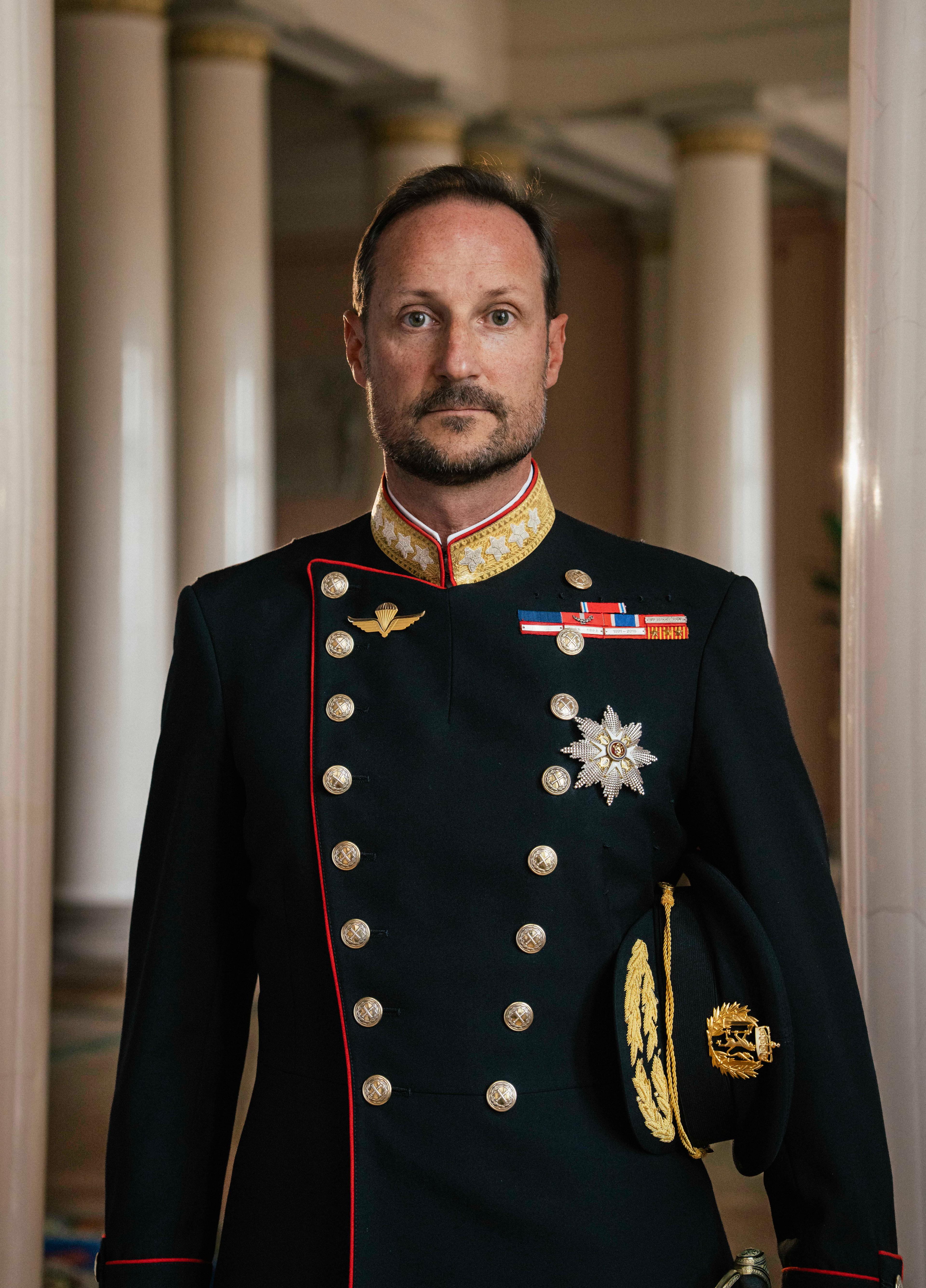Kong Haakon stående i gallauniform med ordener og medaljer.