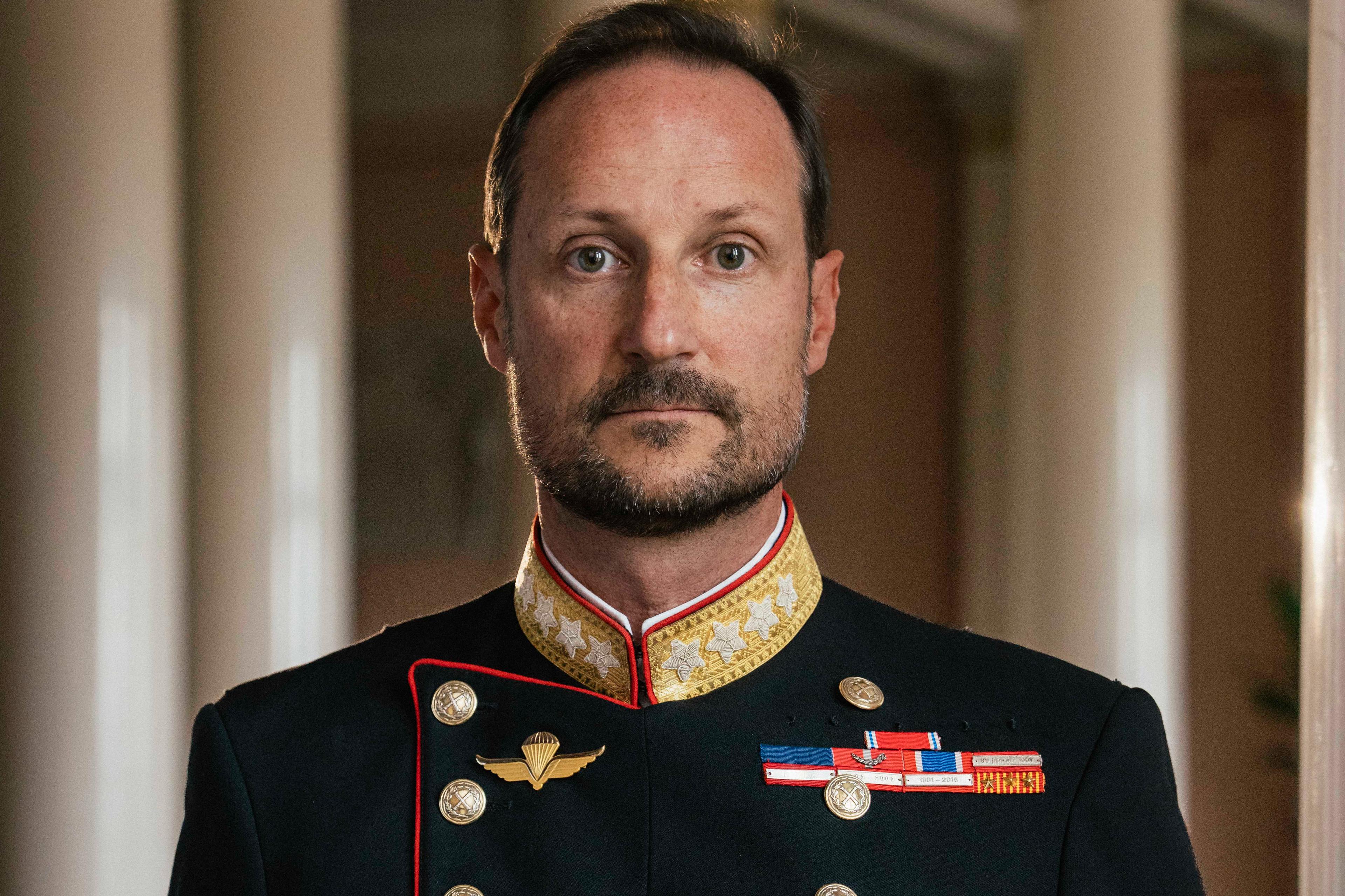Kong Haakon stående i gallauniform med ordener og medaljer.