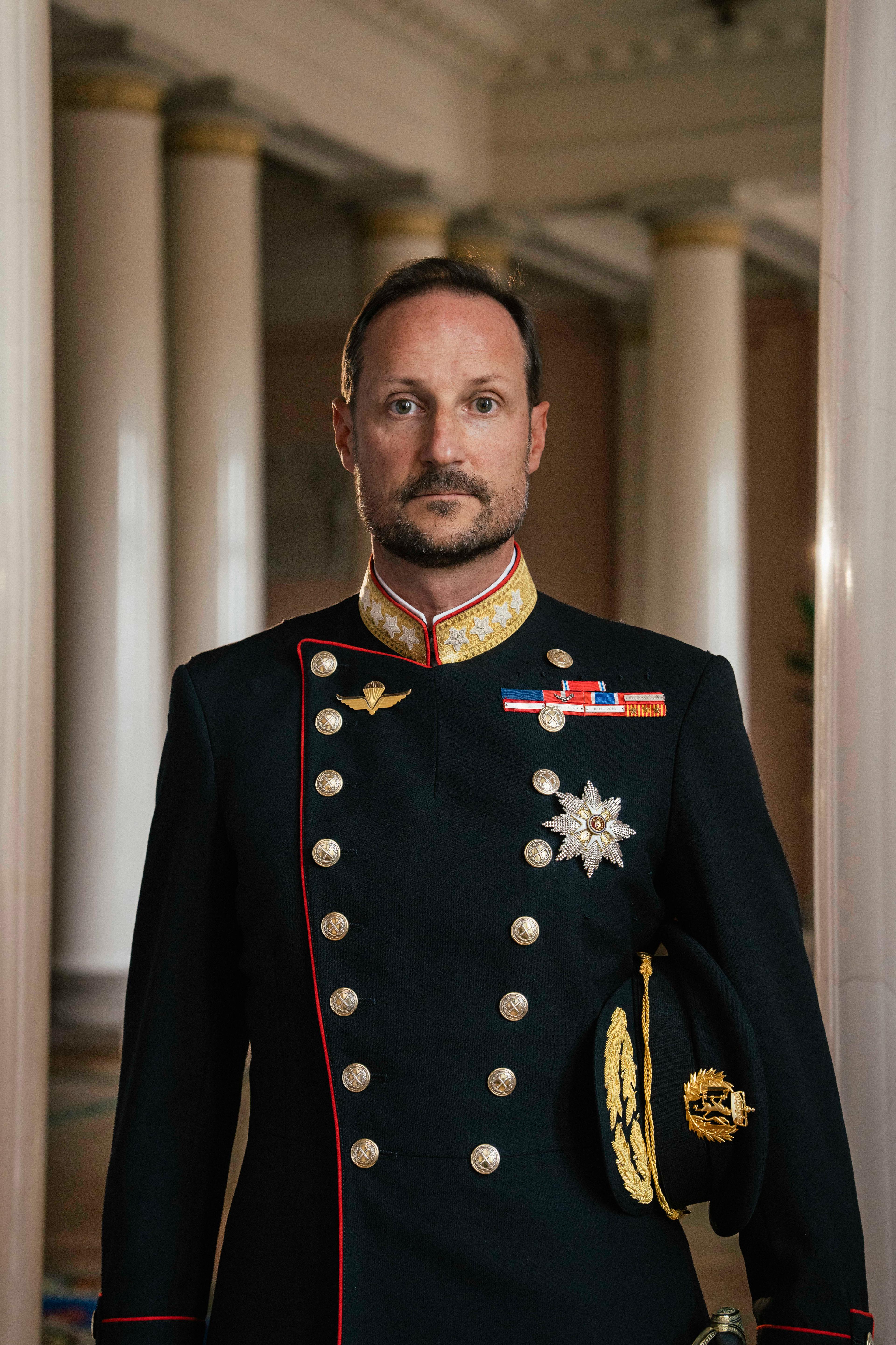 Kong Haakon stående i gallauniform med ordener og medaljer.
