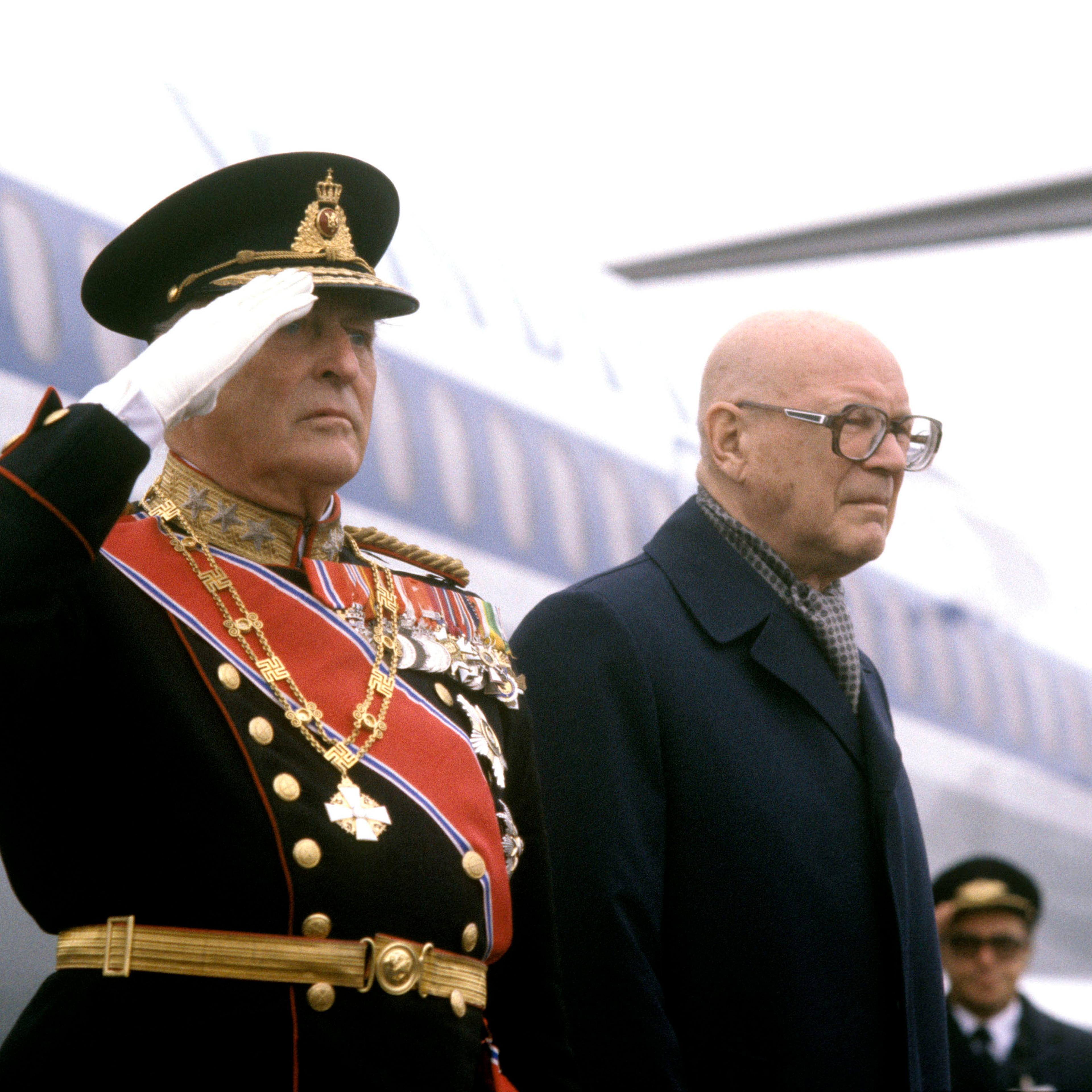 Kong Olav i gallauniform gjør honnør utenfor flyet.