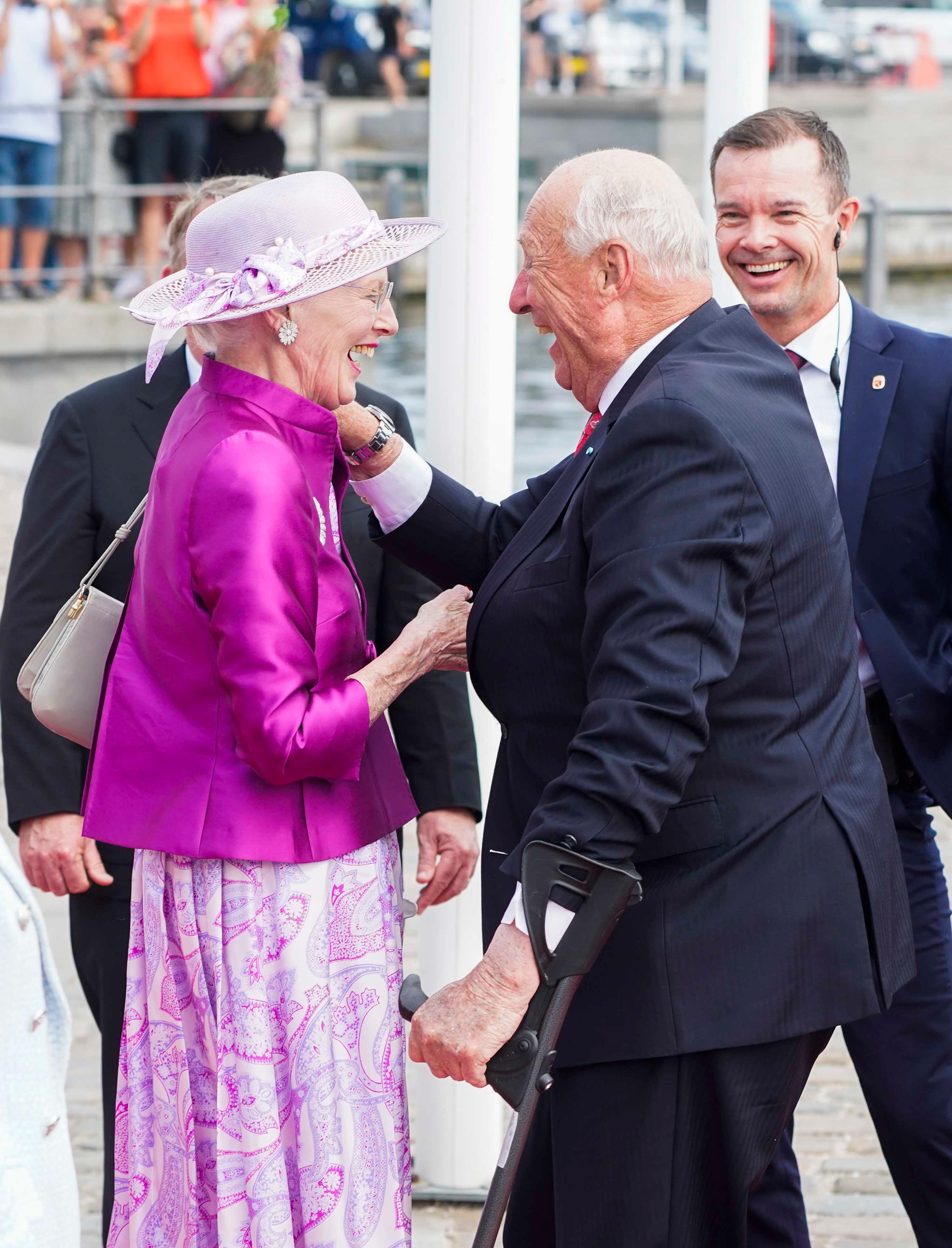 Kong Harald og Dronning Margrethe hilser leende på hverandre.