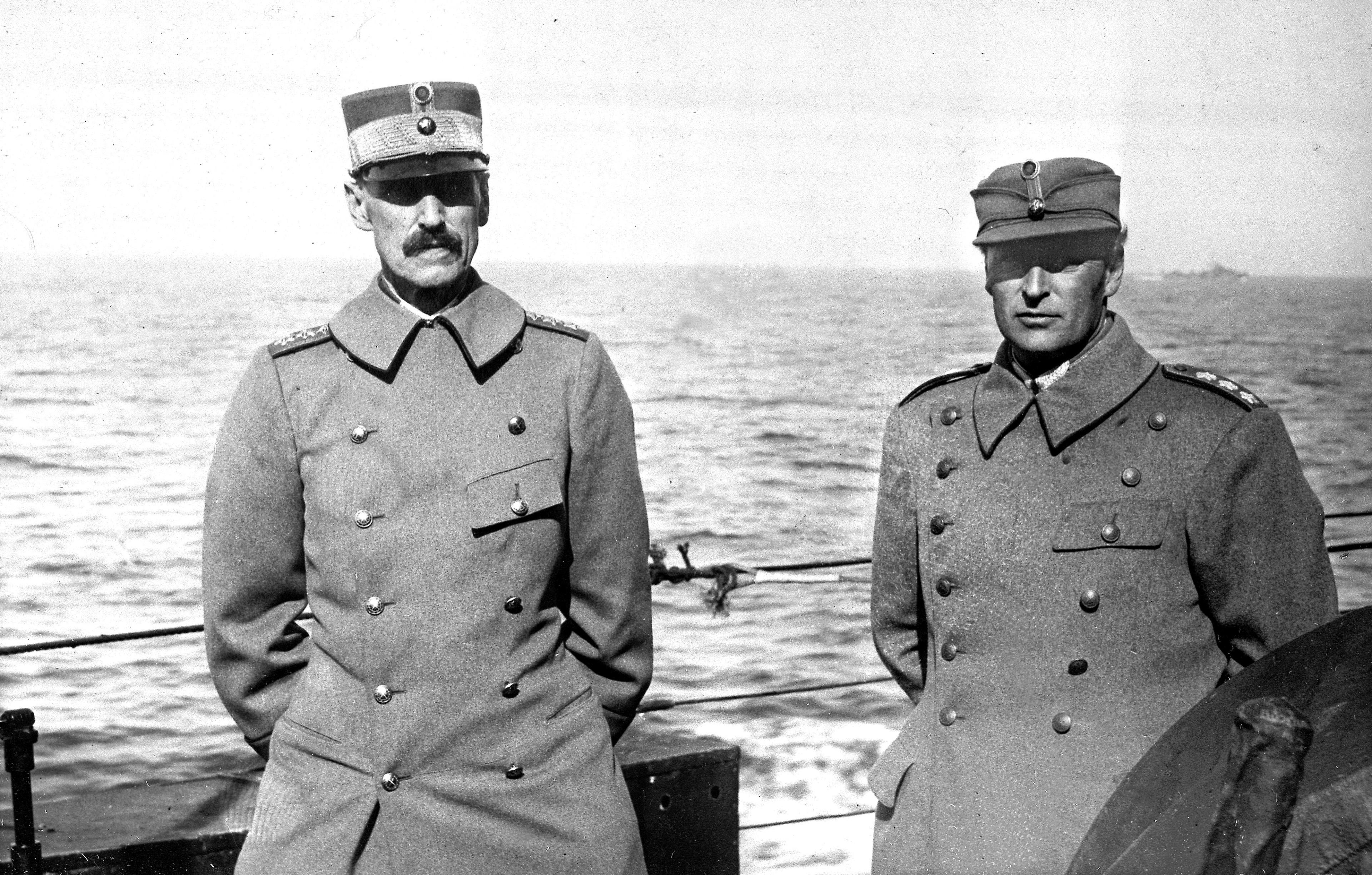 Kong Haakon VII og Kronprins Olav står ved rekka. Begge er i uniform og alvorlige.