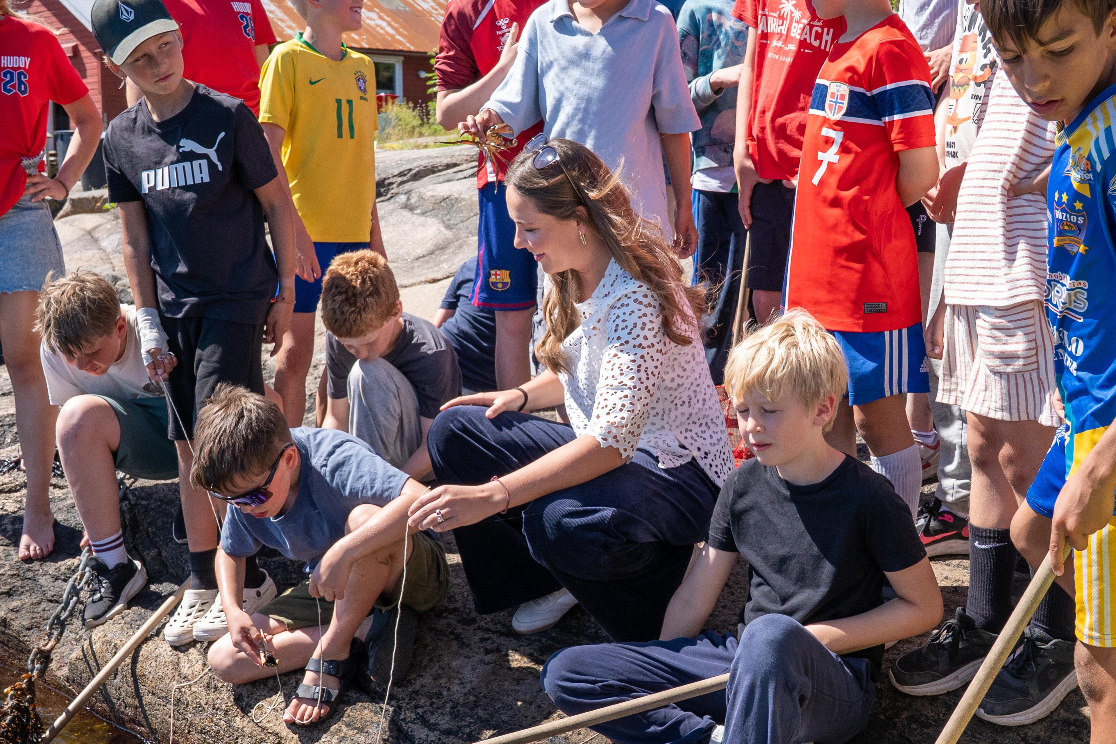 Prinsessen holder et snøre i fjæra. Rundt står gutter i fotballtrøyer, noen med snøre og hov.