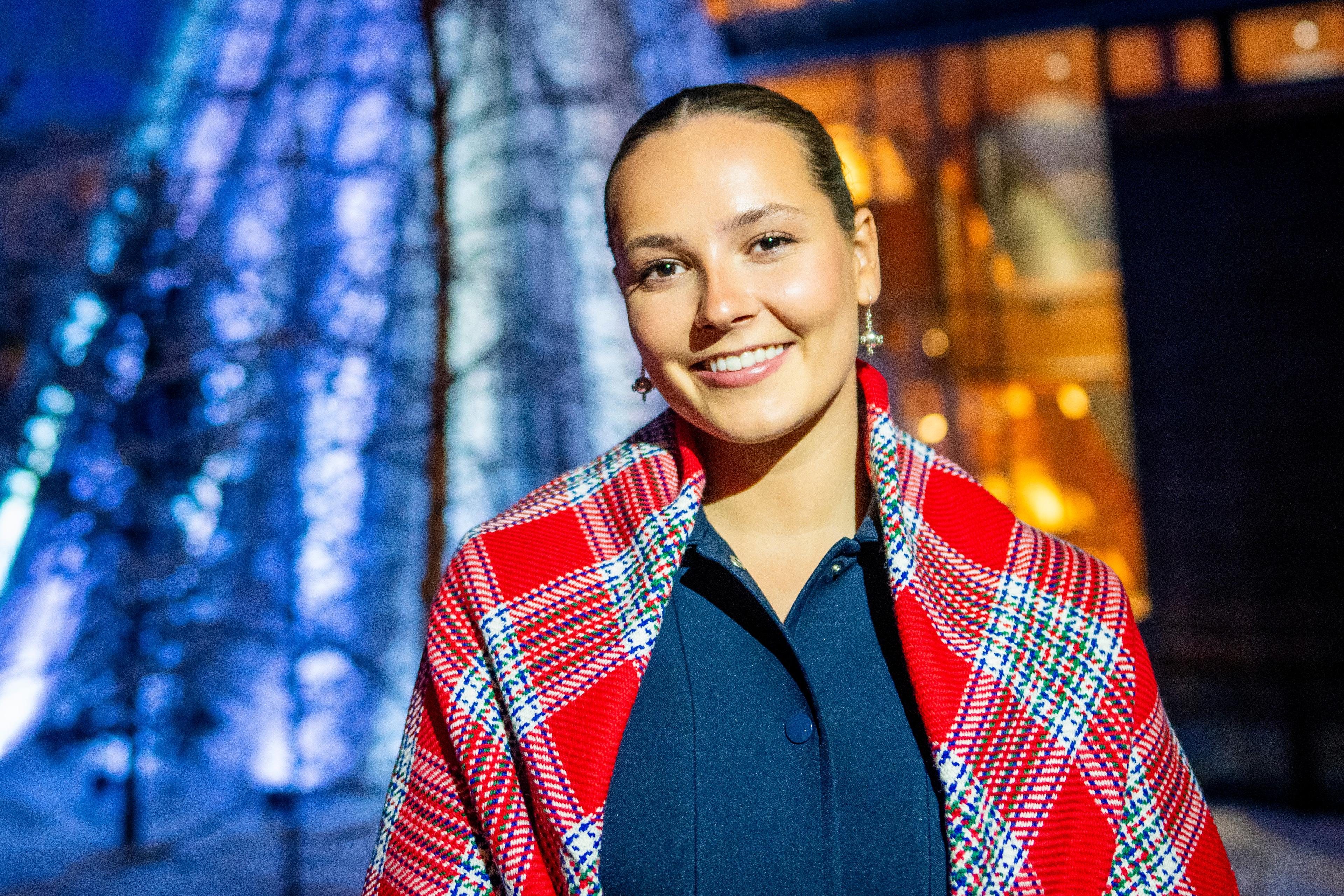 Tett på Prinsesse Ingrid Alexandra i mørke ute, ikledd samisk sjal og med en lyssatt sametingsbygning bak.