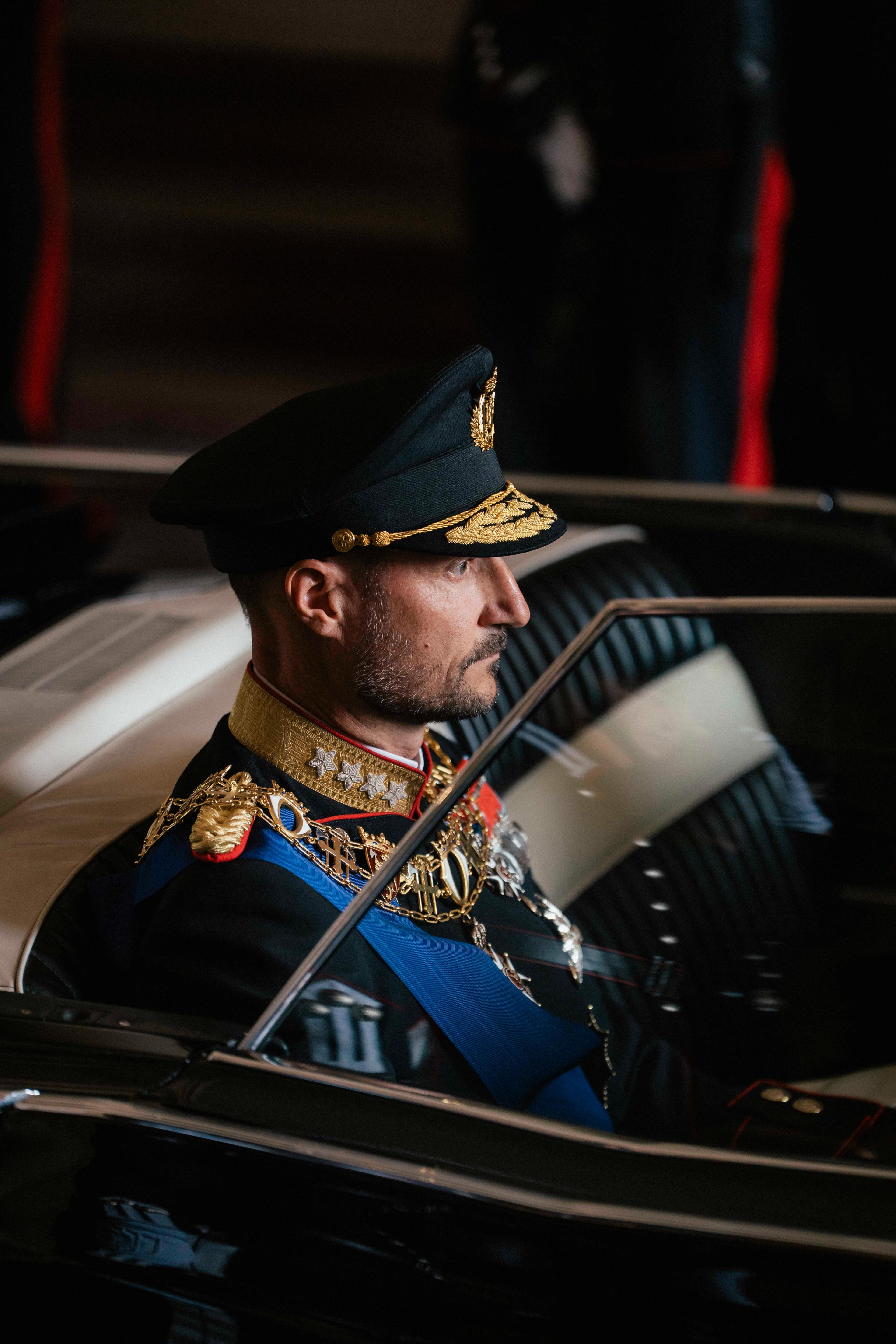 Et nærbilde av Kong Haakon som sitter i den åpne bilen i sin gallauniform.