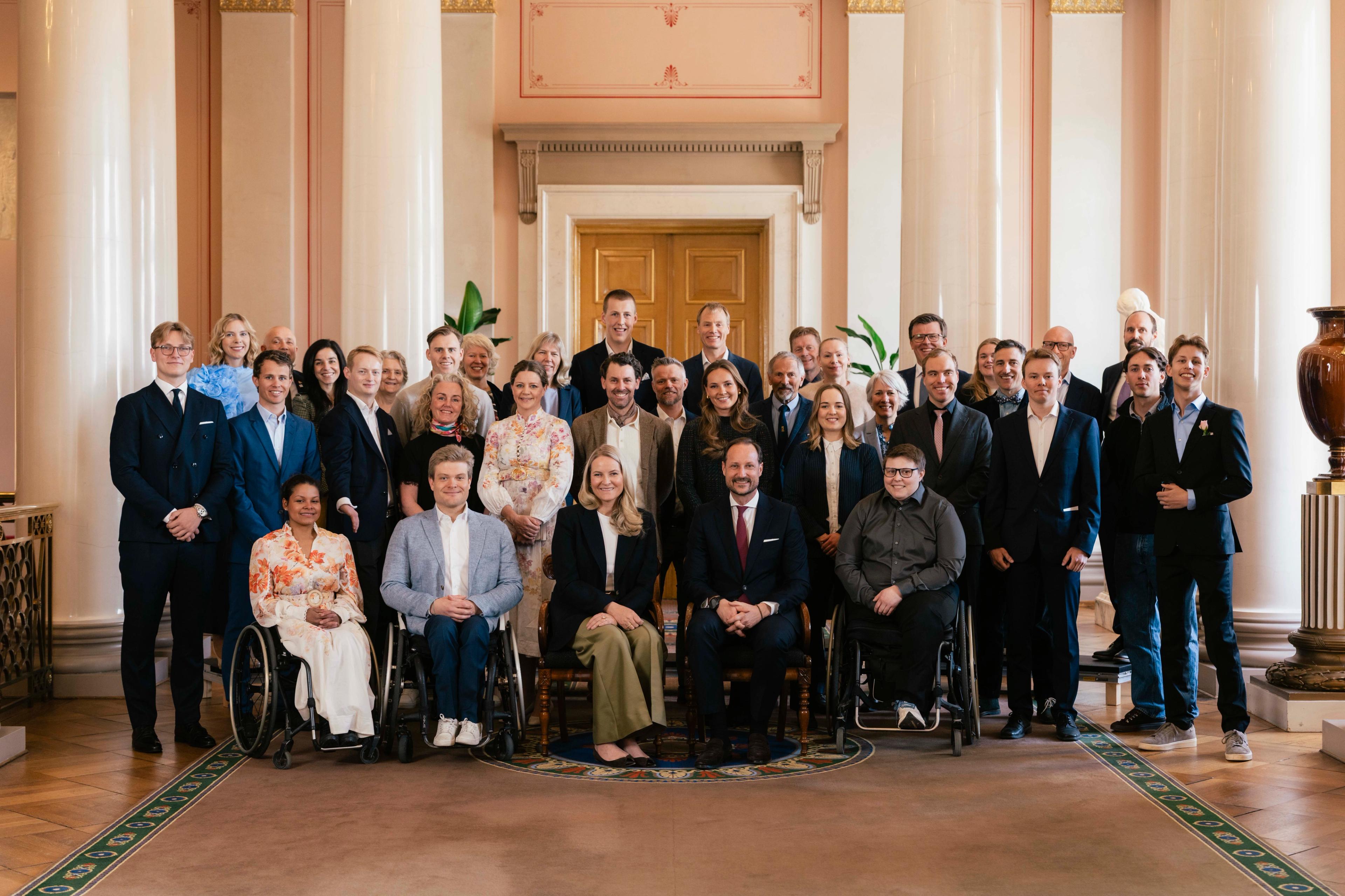 Kronprinsparet sitter på første rad sammen med utøvere i rullestol, mens Prinsesse Ingrid Alexandra og Prins Sverre Magnus står på andre rad sammen med de andre utøverne.