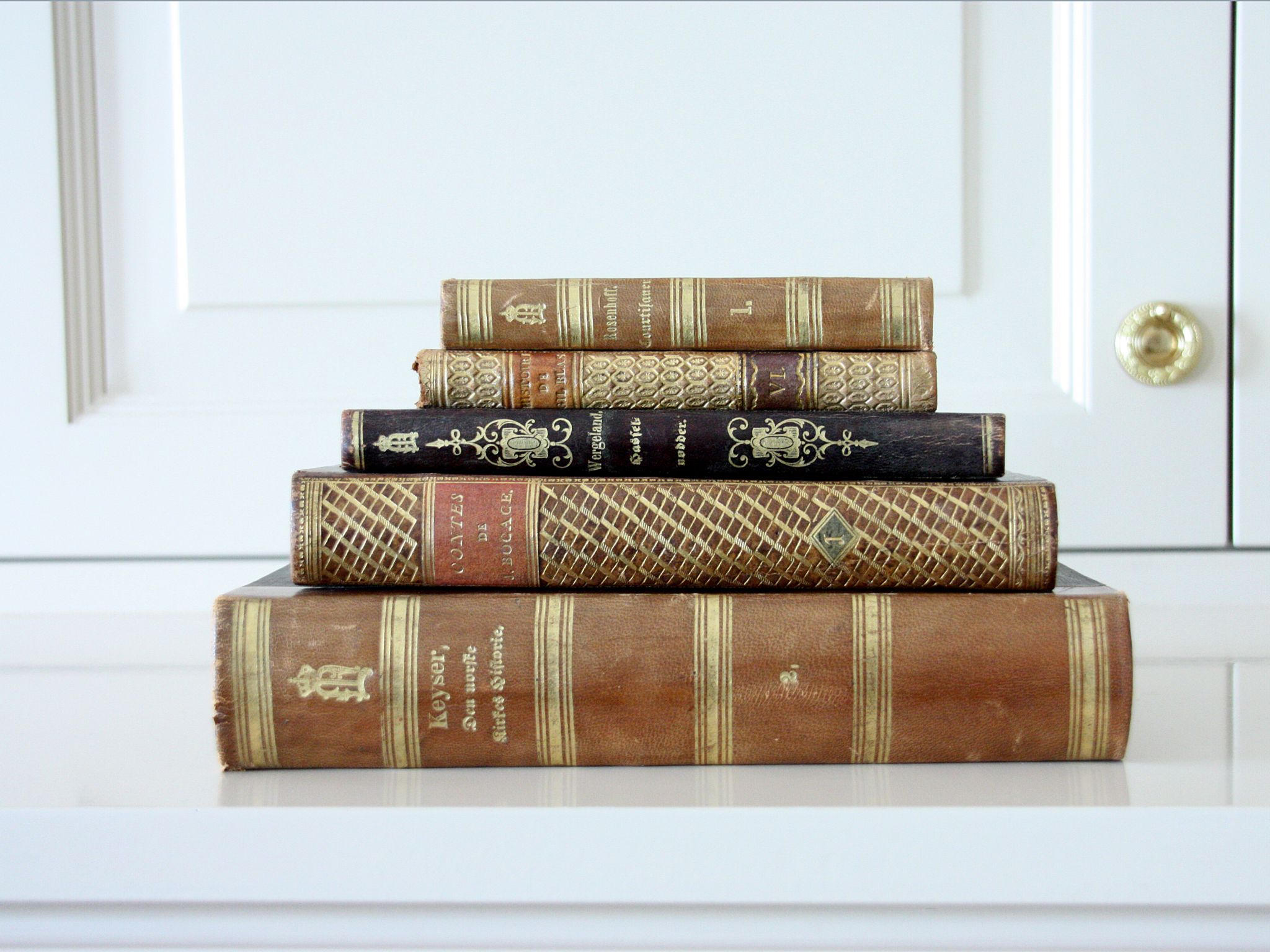 En liten stabel vakkert innbundne bøker ligger på en hvit hylle med ryggene mot oss.
