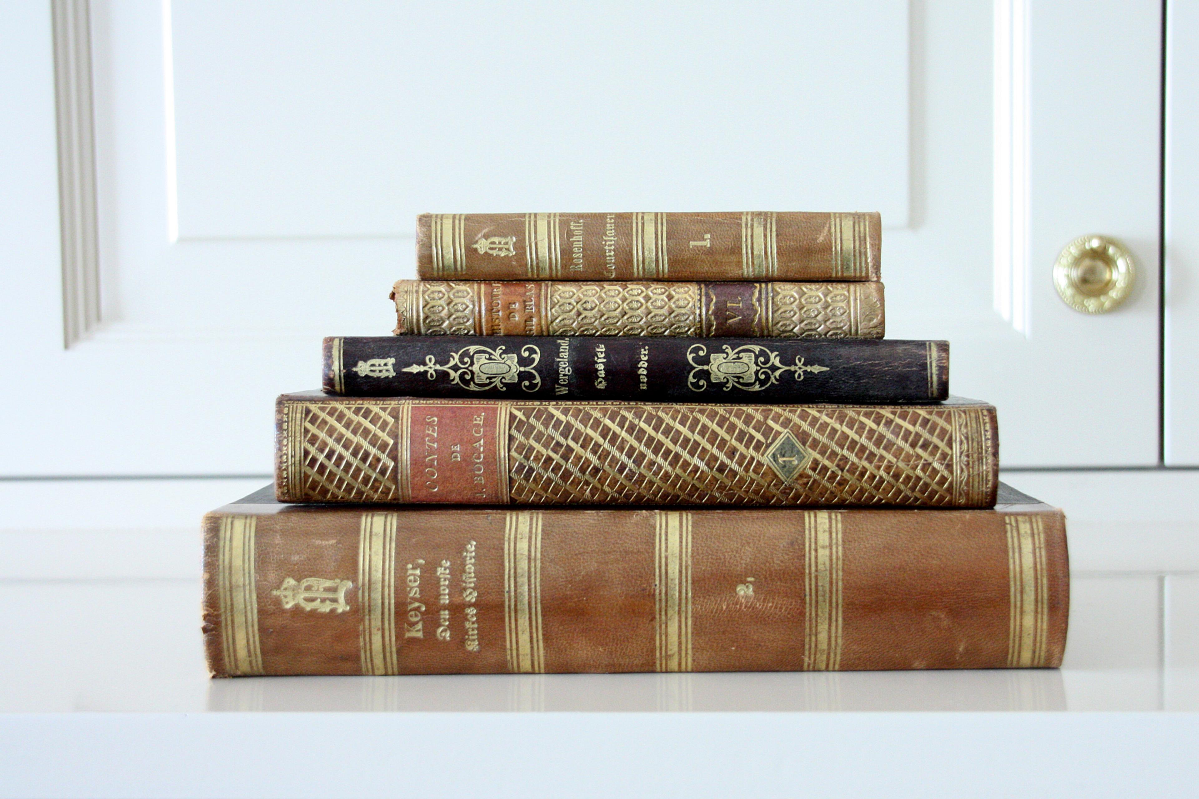 En liten stabel vakkert innbundne bøker ligger på en hvit hylle med ryggene mot oss.