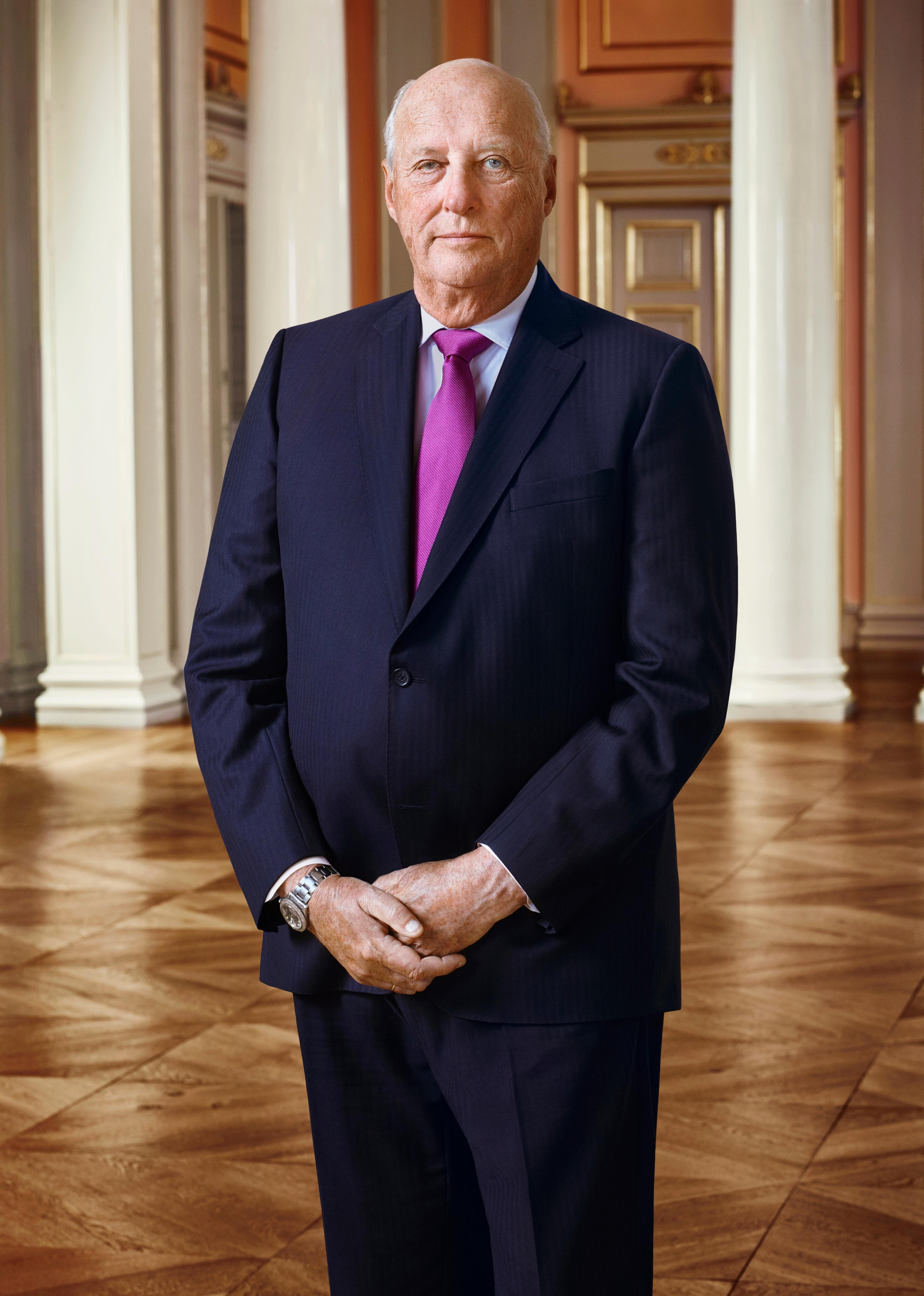 Portrett av Kong Harald i halvfigur. Kongen har mørk dress, hvit skjorte og lilla slips.