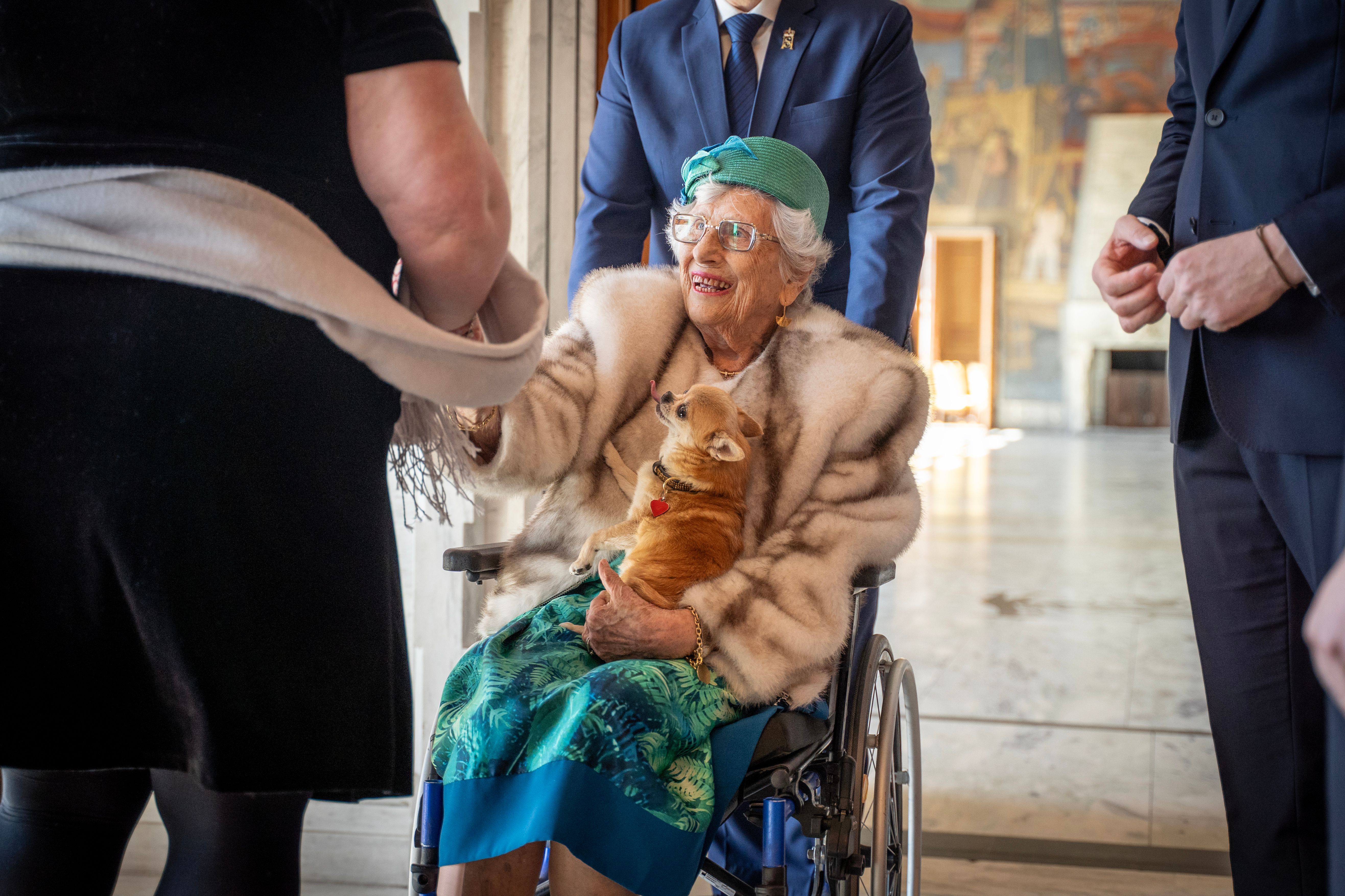 Prinsesse Astrid sitter i en rullestol med hunden Wilma på fanget. Hun rekker ut en hånd til styreleder Kathrin Dahlstrøm, som står med ryggen til.