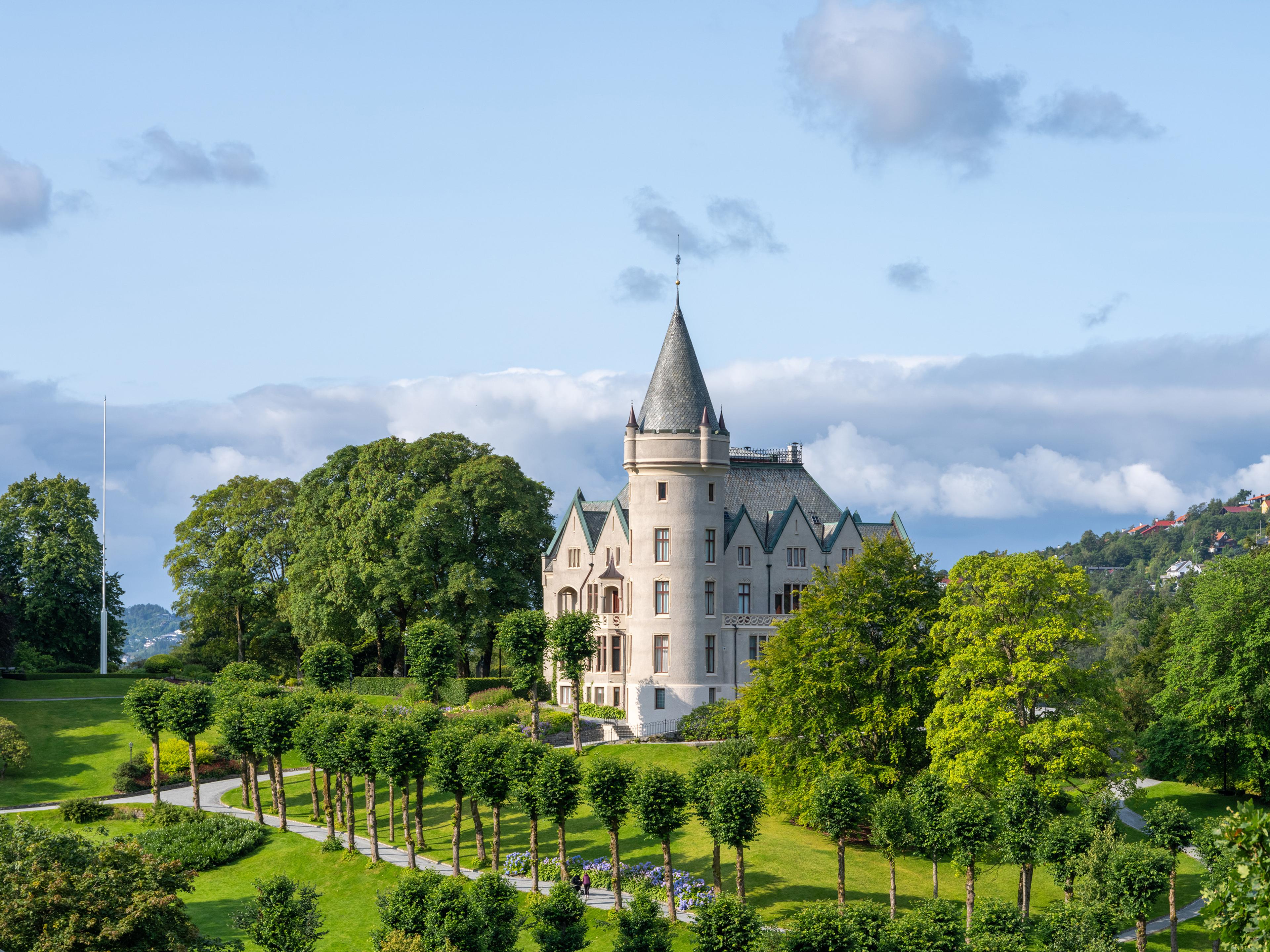 En grå herskapsbolig med tårn, omgitt av en vakker park.