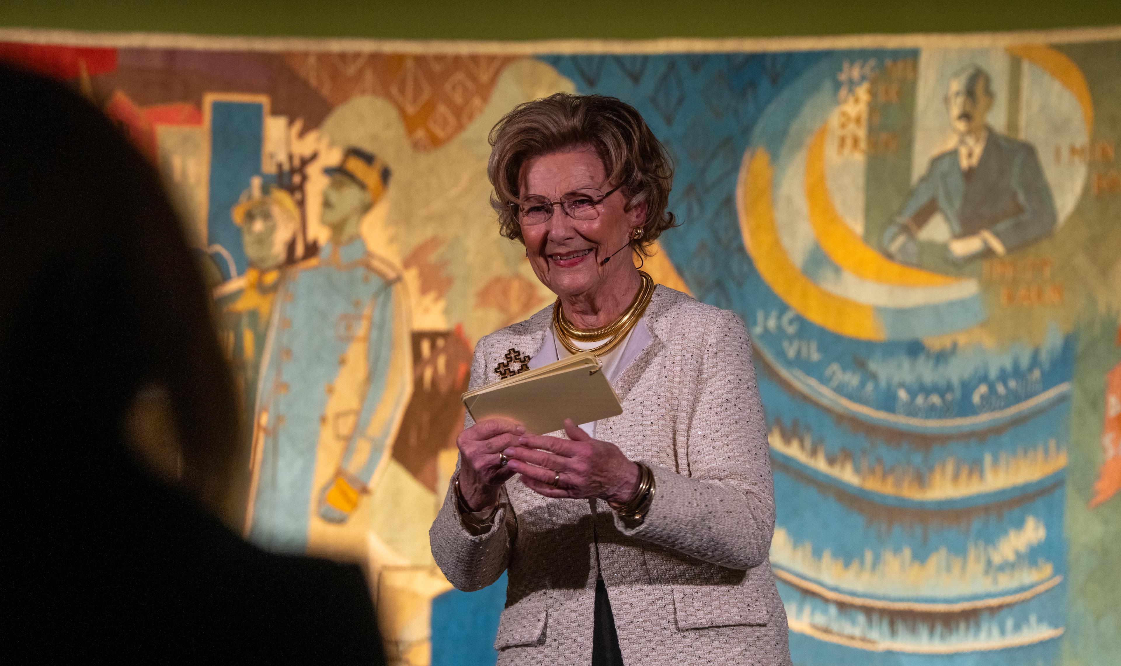Dronning Sonja på scenen med Kongeteppet i bakgrunnen.