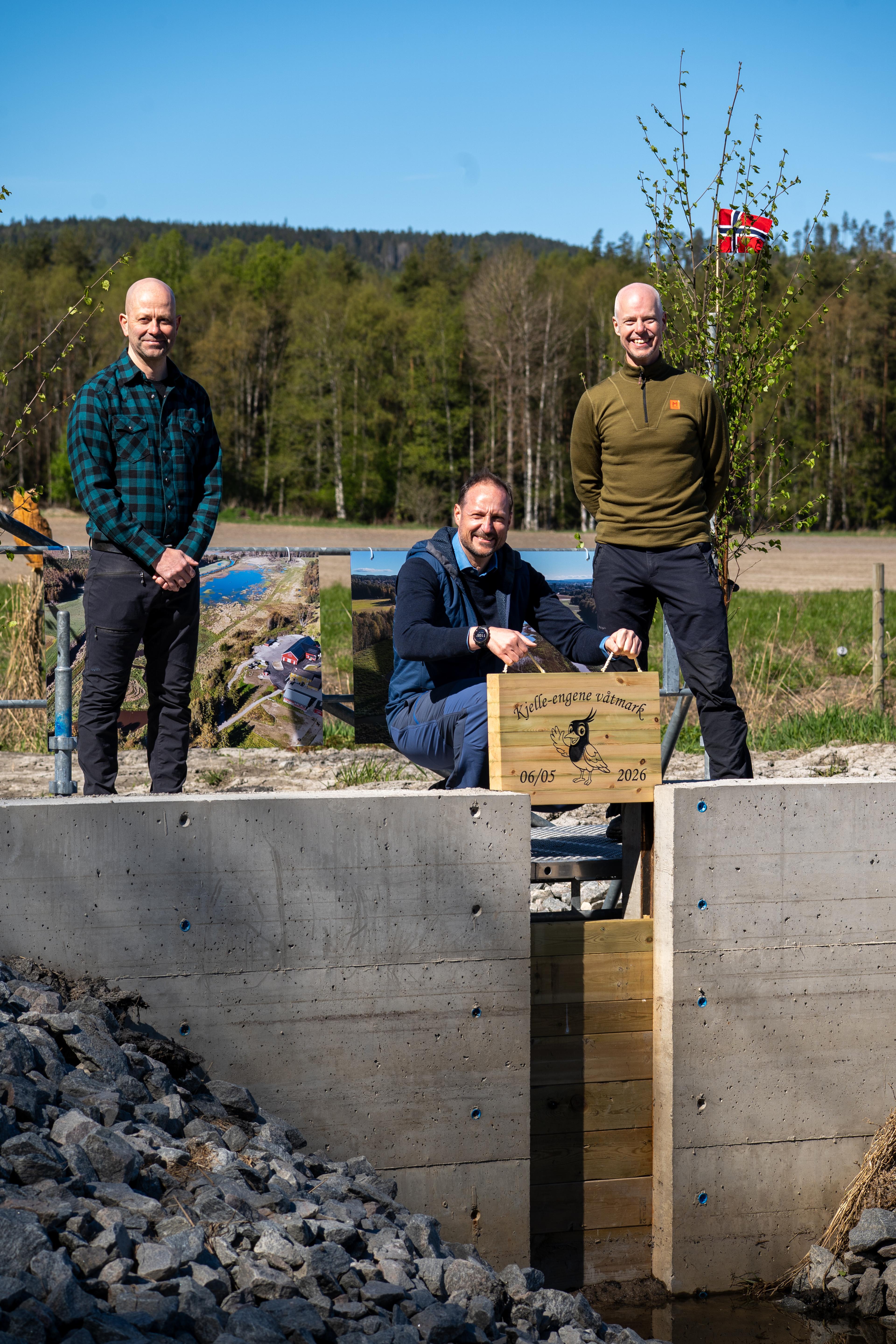 Kronprins Haakon på huk med planken i hendene, med våtmarkskameratene smilende på hver side.