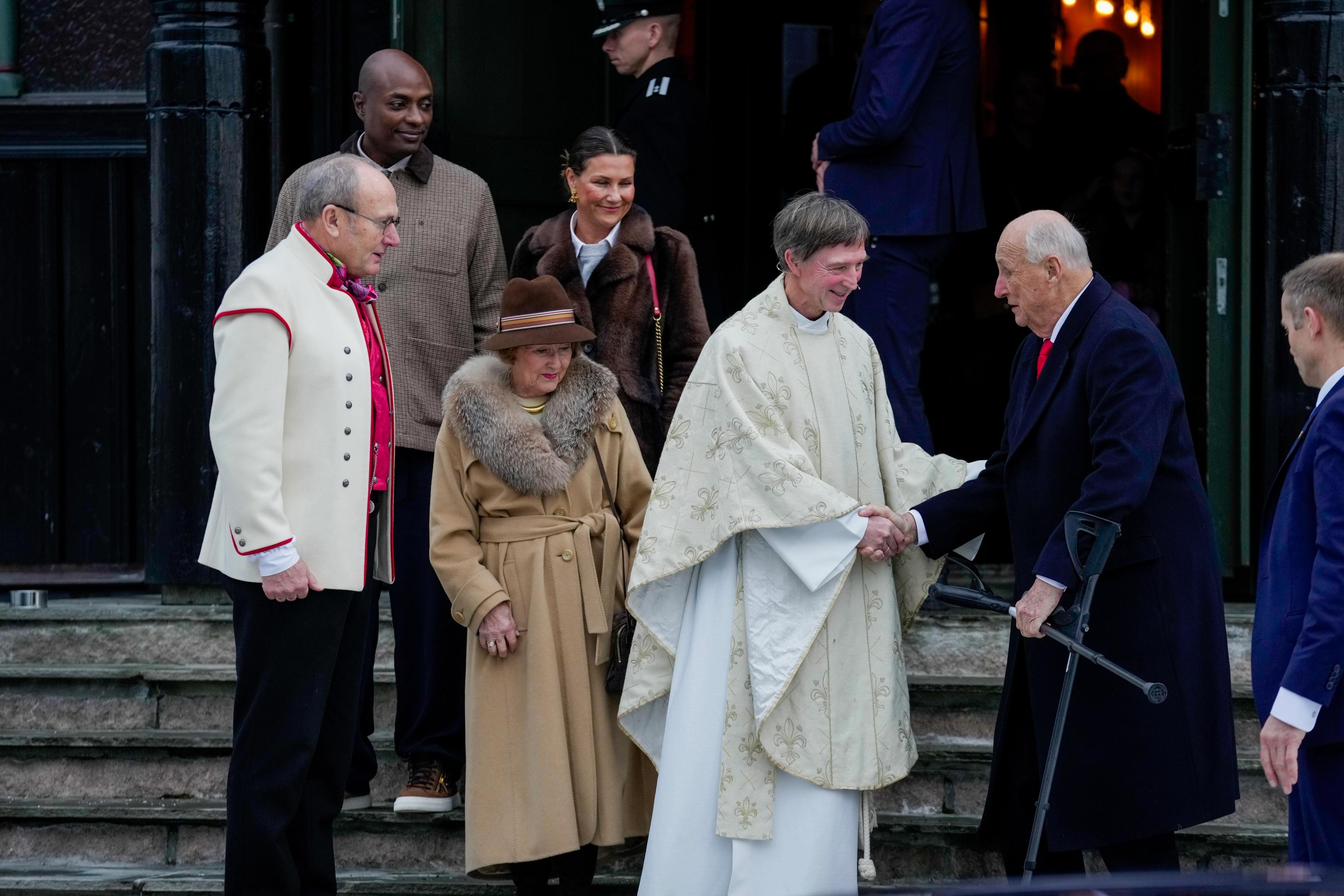 Kong Harald og soknepresten tek kvarandre i handa på kyrkjetrappa. Fleire følgjer på.