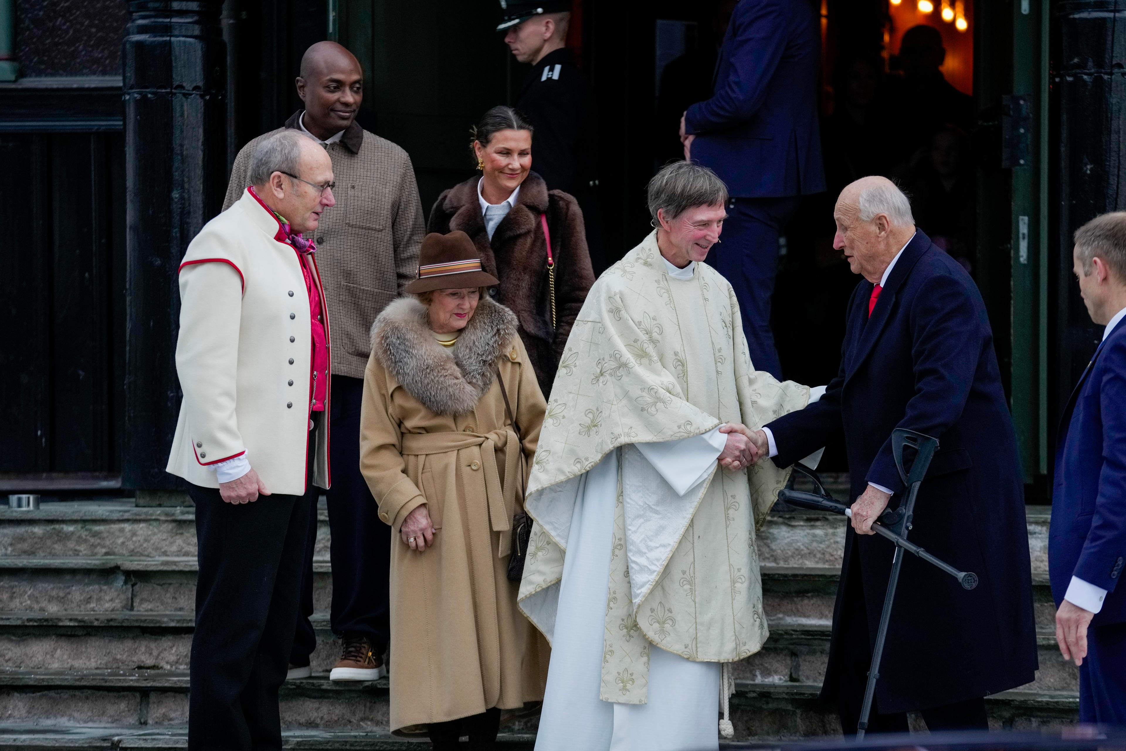 Kong Harald og soknepresten tek kvarandre i handa på kyrkjetrappa. Fleire følgjer på.