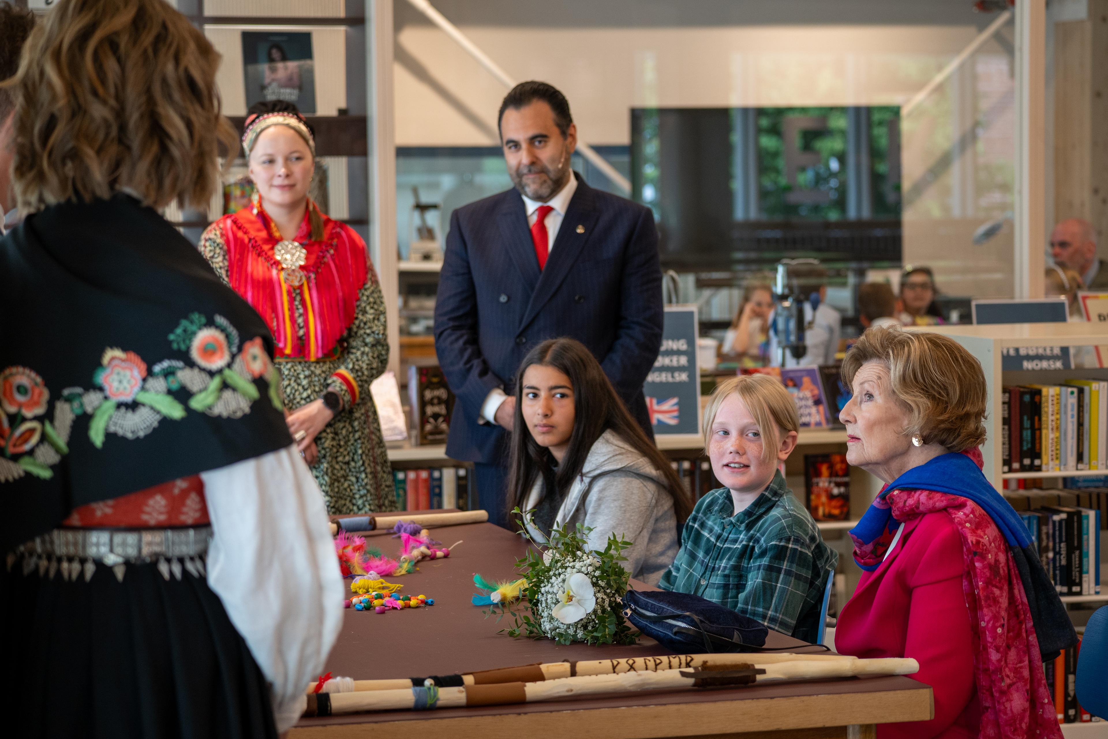 Dronning Sonja og femteklassingar sit rundt eit bord.