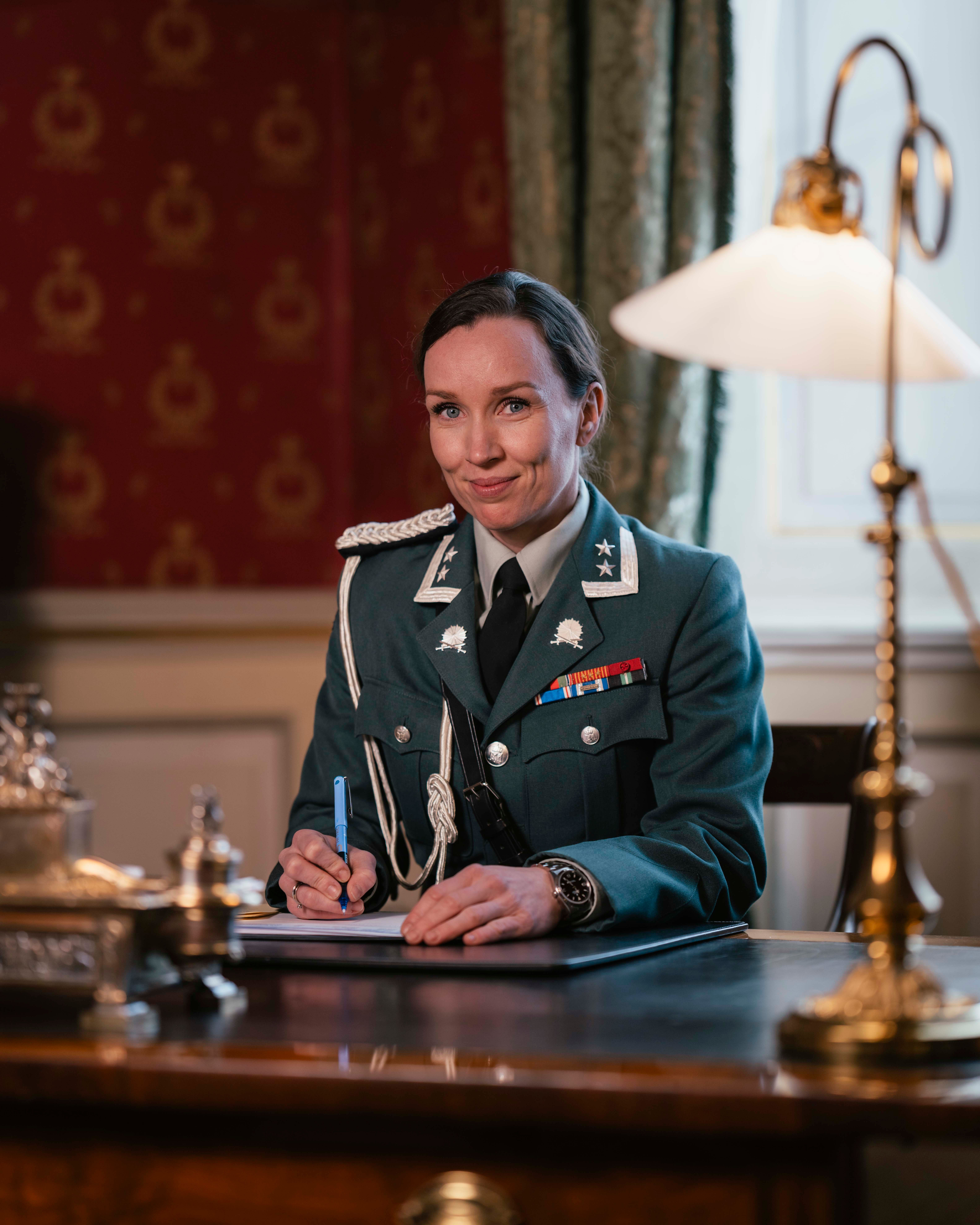 En kvinnelig adjutant sitter ved skrivebordet iført hærens uniform.
