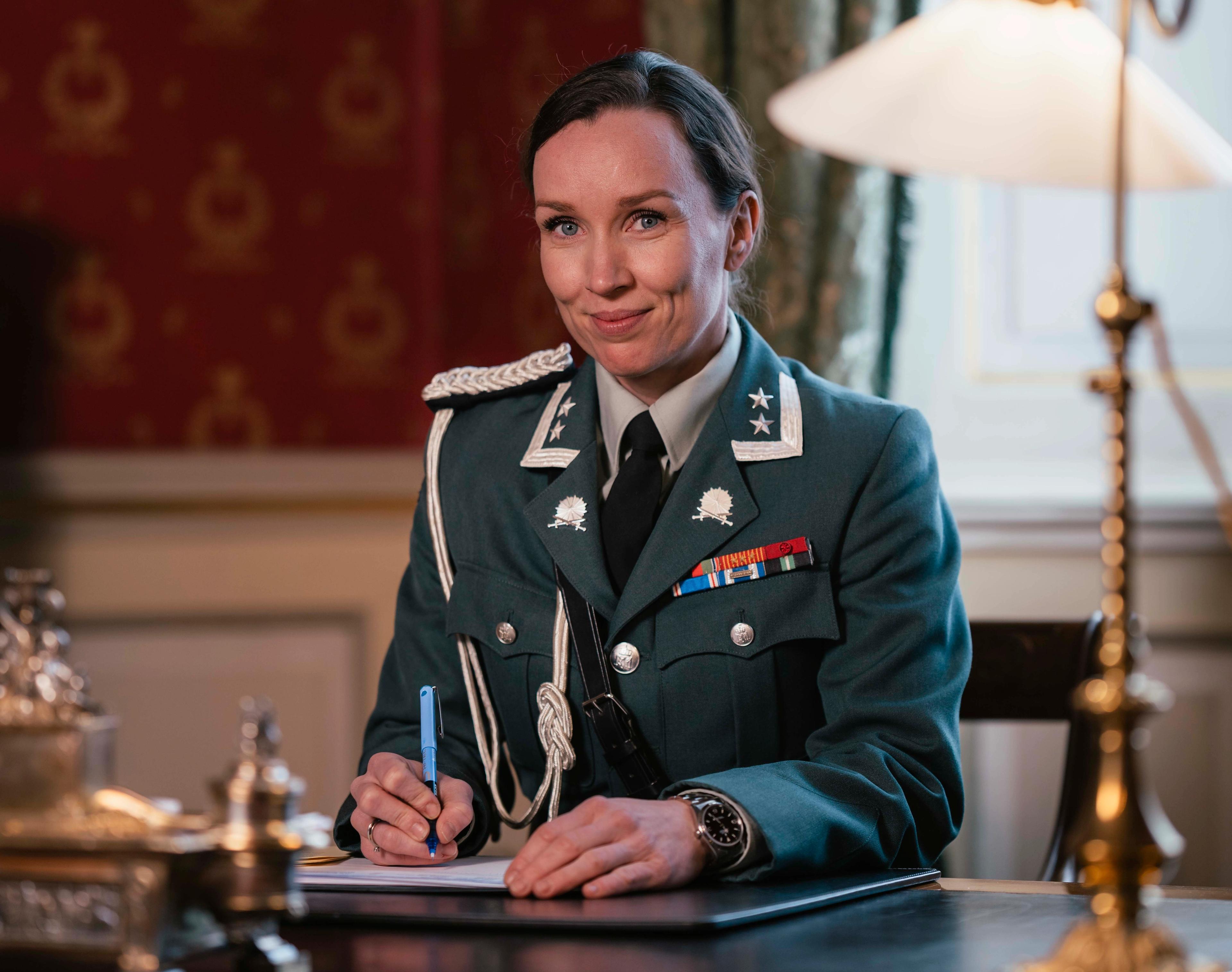 En kvinnelig adjutant sitter ved skrivebordet iført hærens uniform.