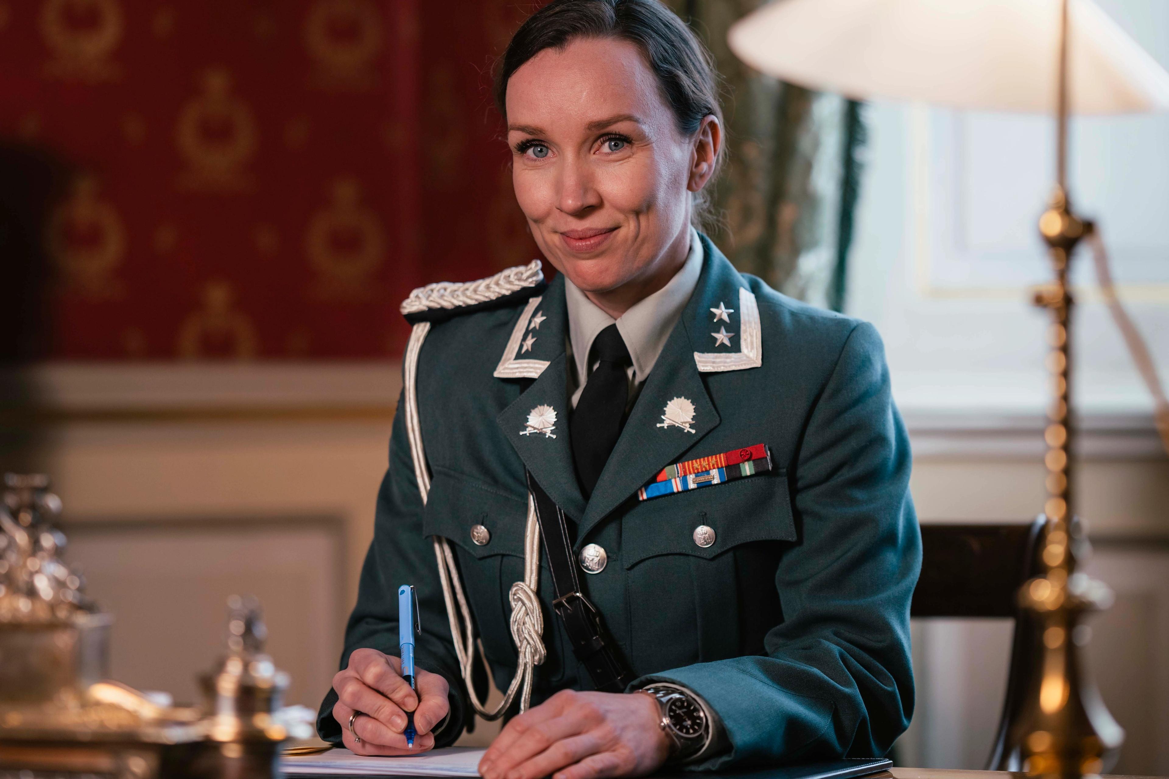 En kvinnelig adjutant sitter ved skrivebordet iført hærens uniform.