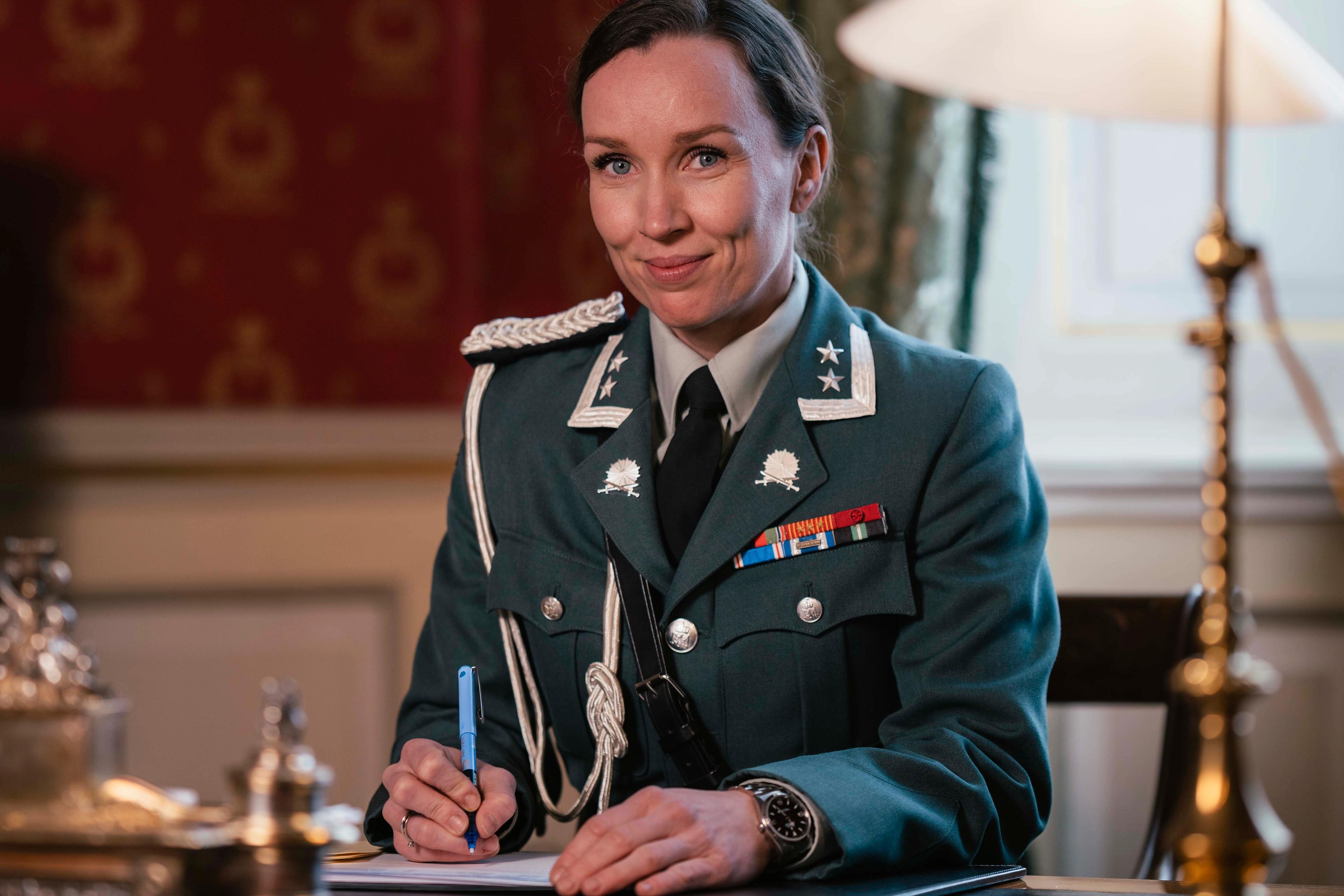 En kvinnelig adjutant sitter ved skrivebordet iført hærens uniform.