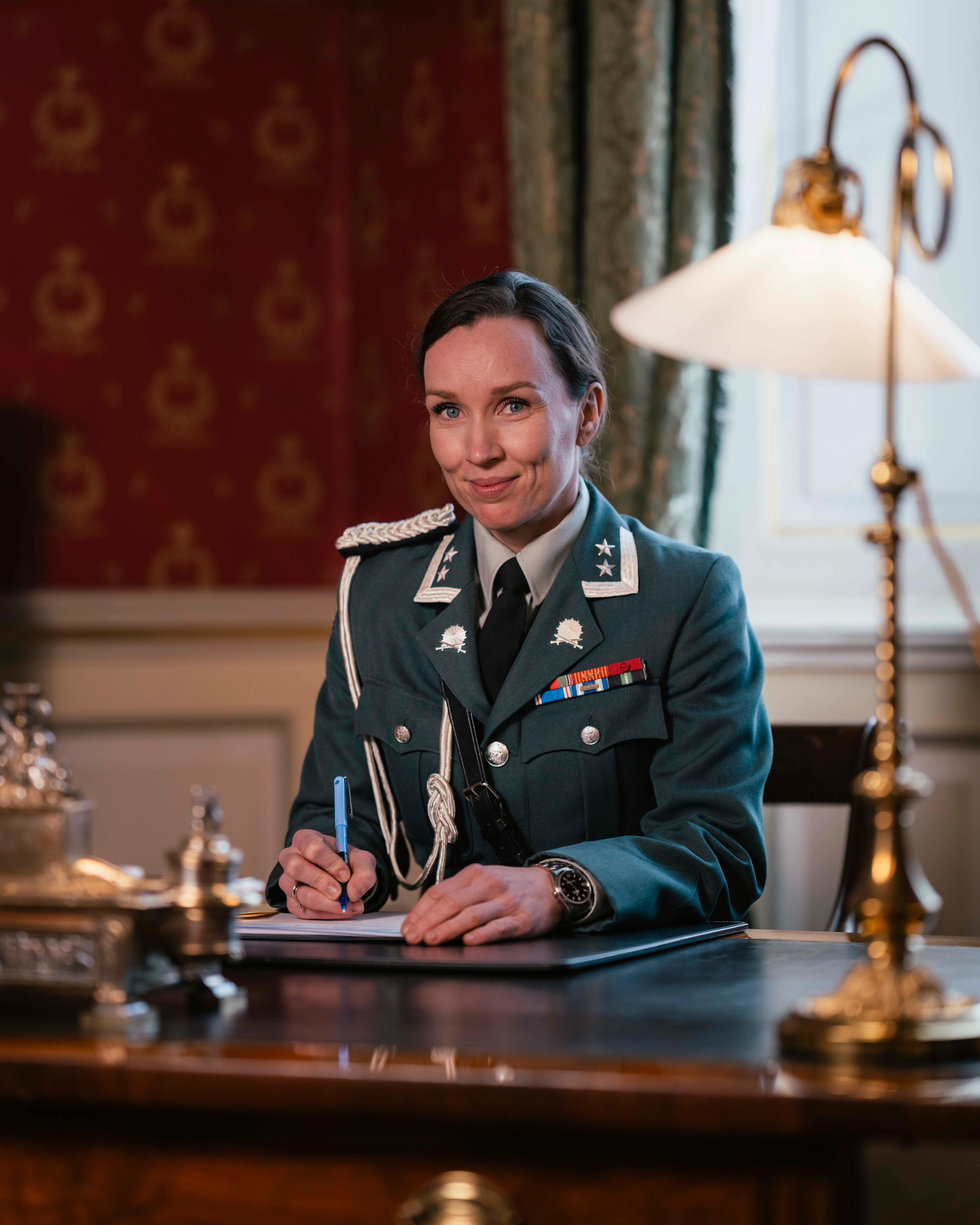 En kvinnelig adjutant sitter ved skrivebordet iført hærens uniform.