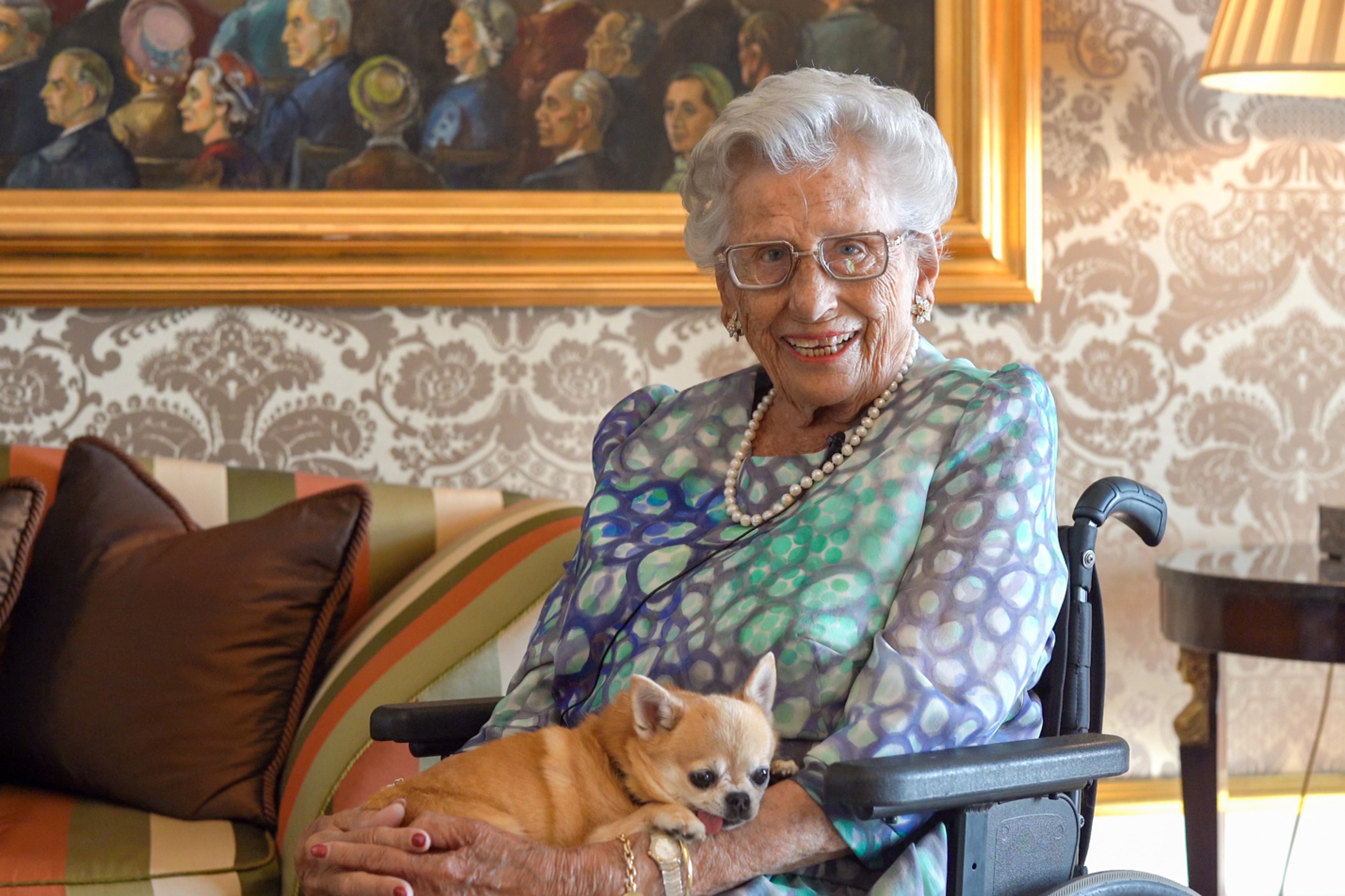 Prinsesse Astrid sitter med hunden sin i fanget og smiler mot kameraet.