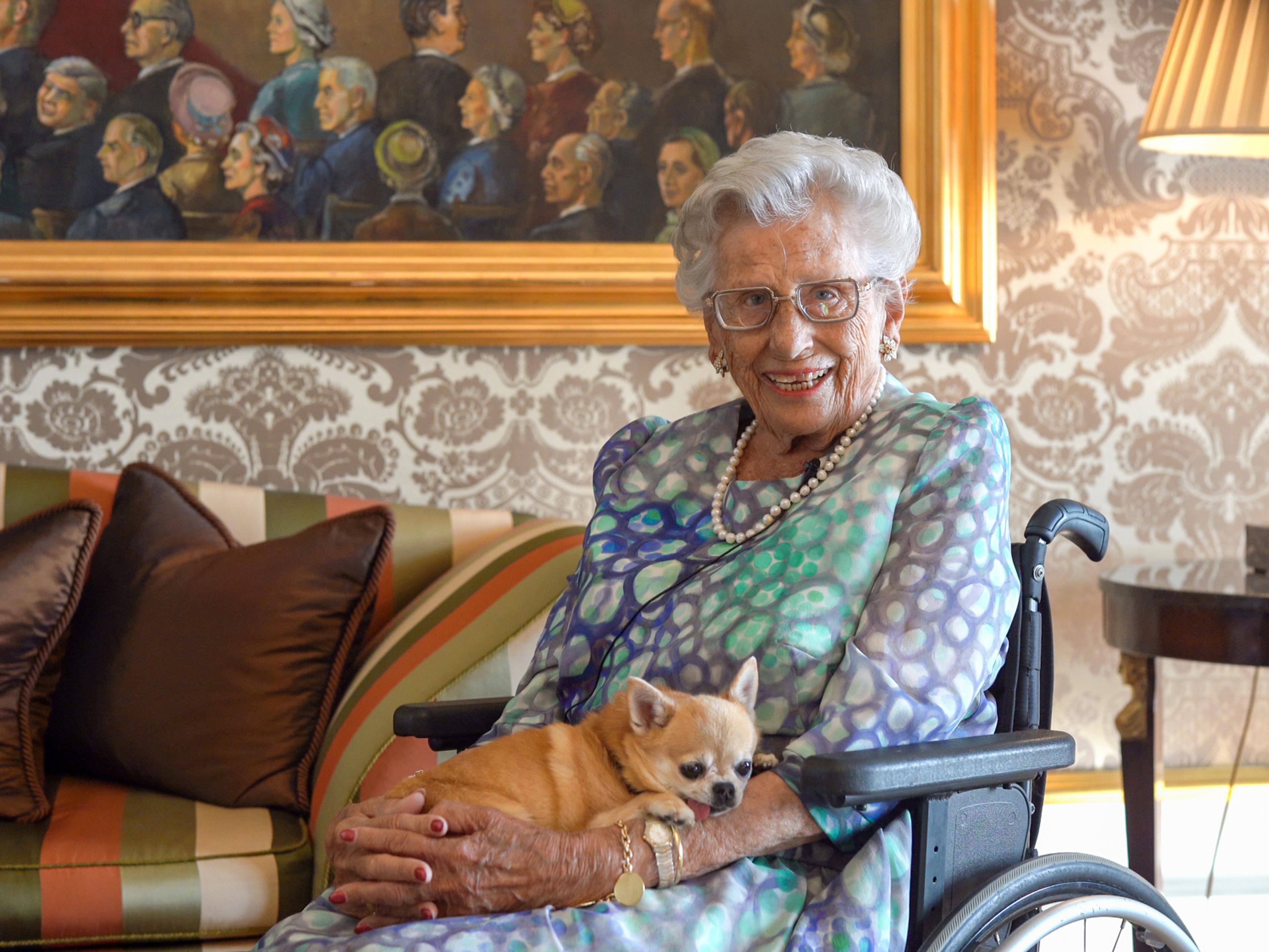 Prinsesse Astrid sitter med hunden sin i fanget og smiler mot kameraet.