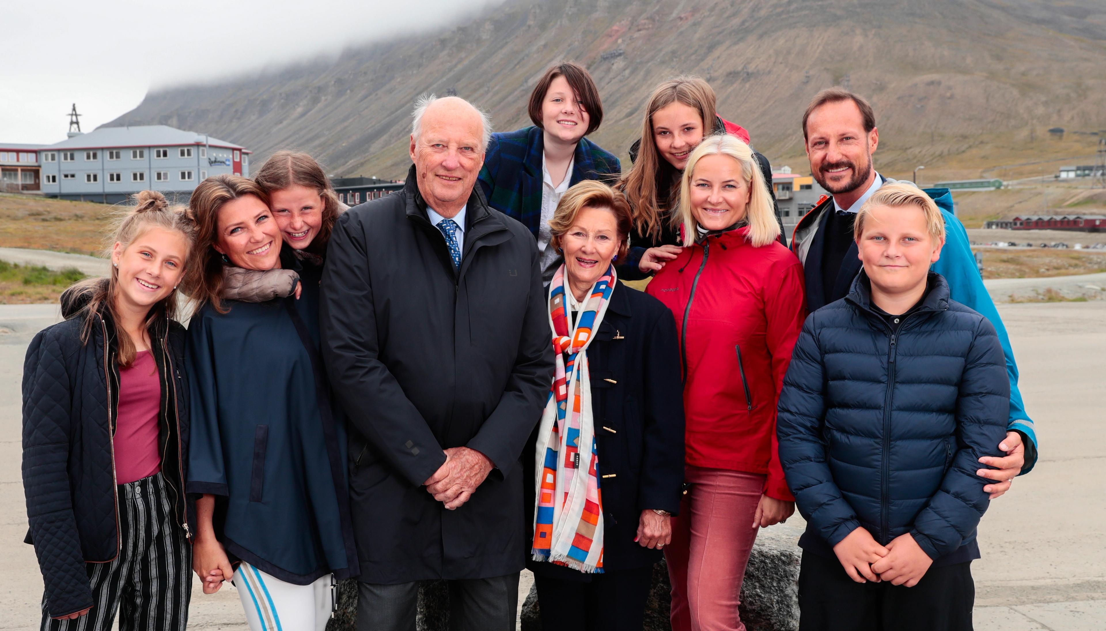 Kong Harald og Dronning Sonja med barn og barnebarn rundt seg og Longyearbyen i bakgrunnen.