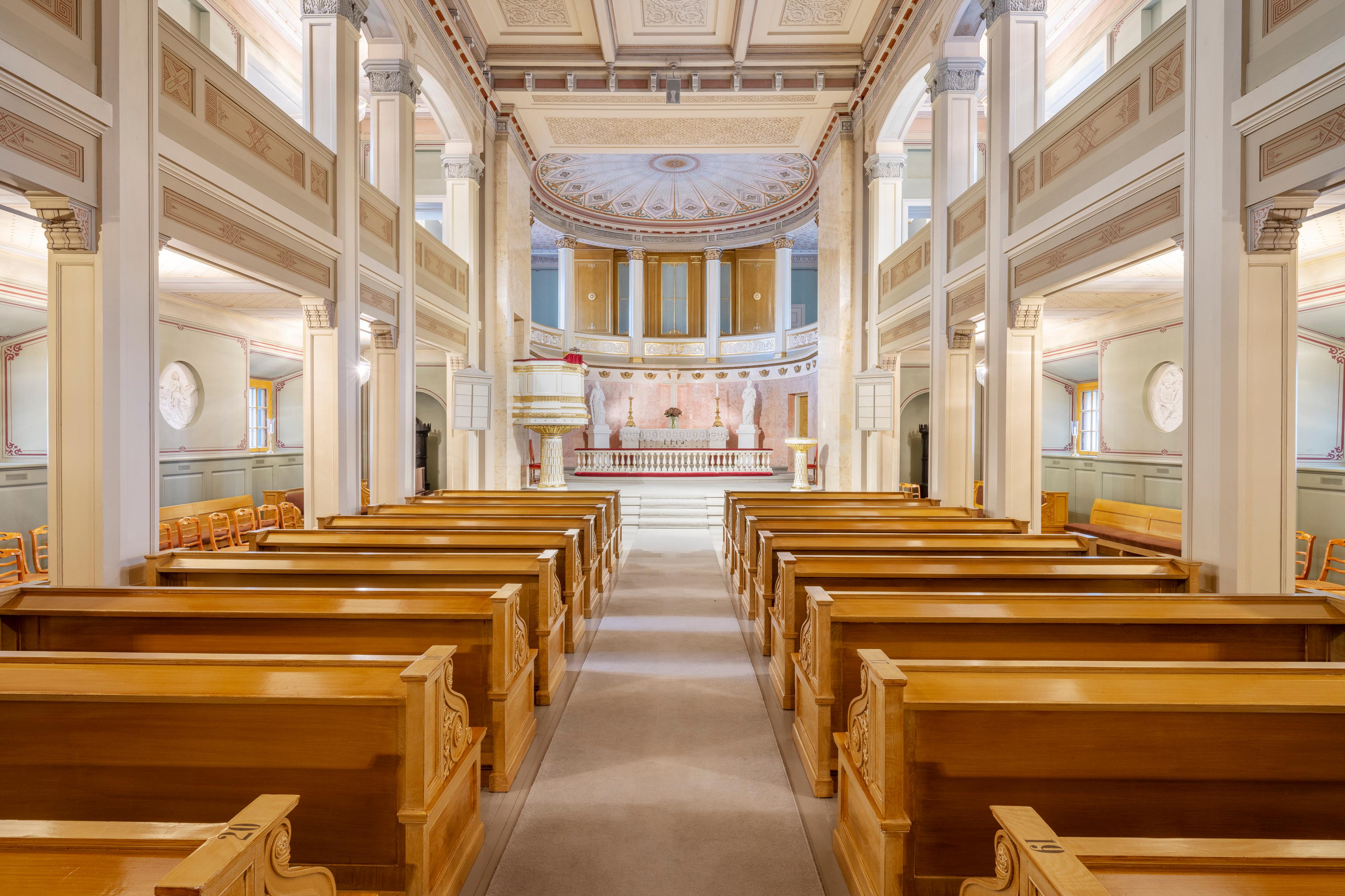 Slottskapellet fotografert fra inngangen. Benkeradene strekker seg innover i rommet, som er lyst og går over to etasjer med søyler og gallerier. Fremst ligger alteret, med et vakkert utsmykket tak over.