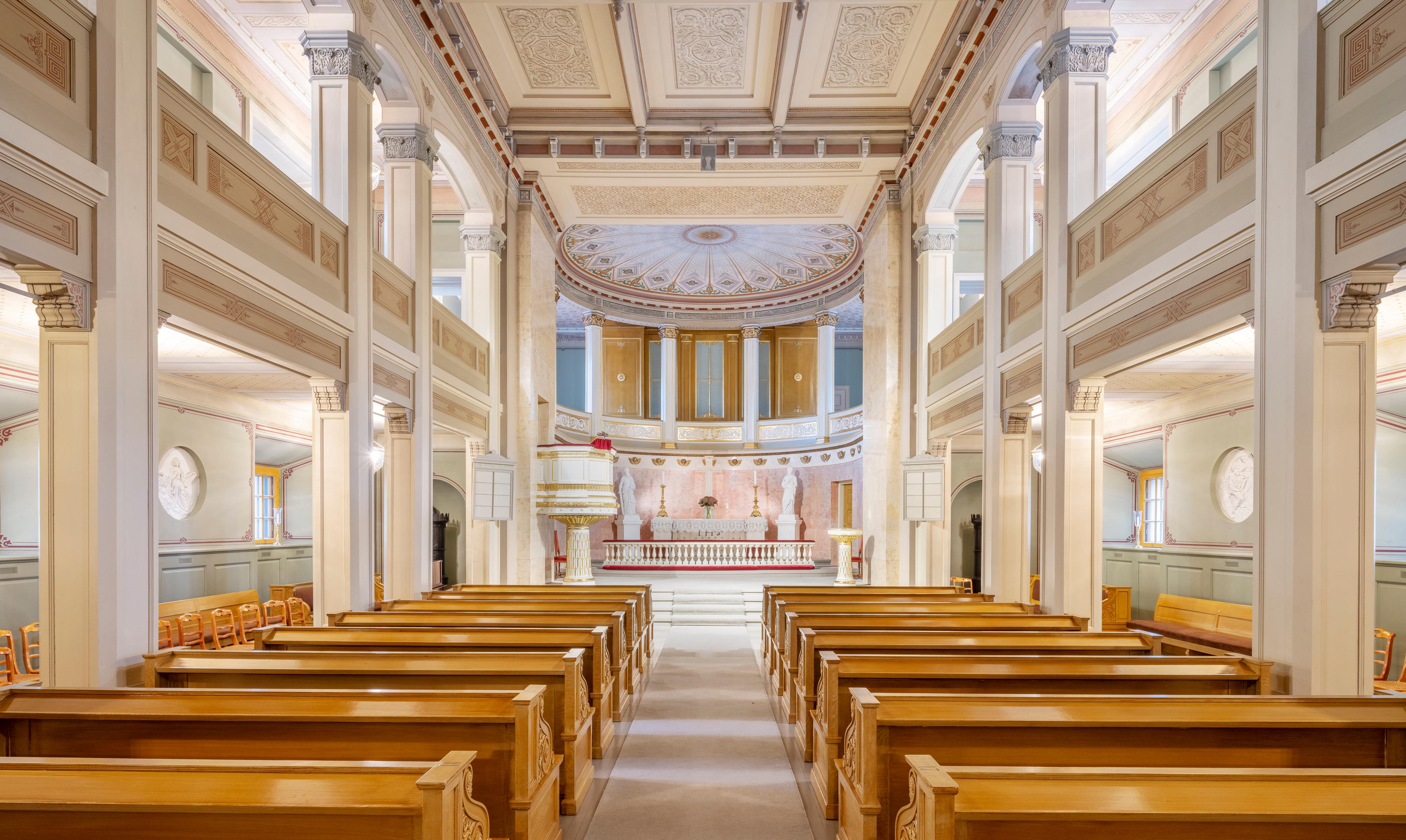 Slottskapellet fotografert fra inngangen. Benkeradene strekker seg innover i rommet, som er lyst og går over to etasjer med søyler og gallerier. Fremst ligger alteret, med et vakkert utsmykket tak over.