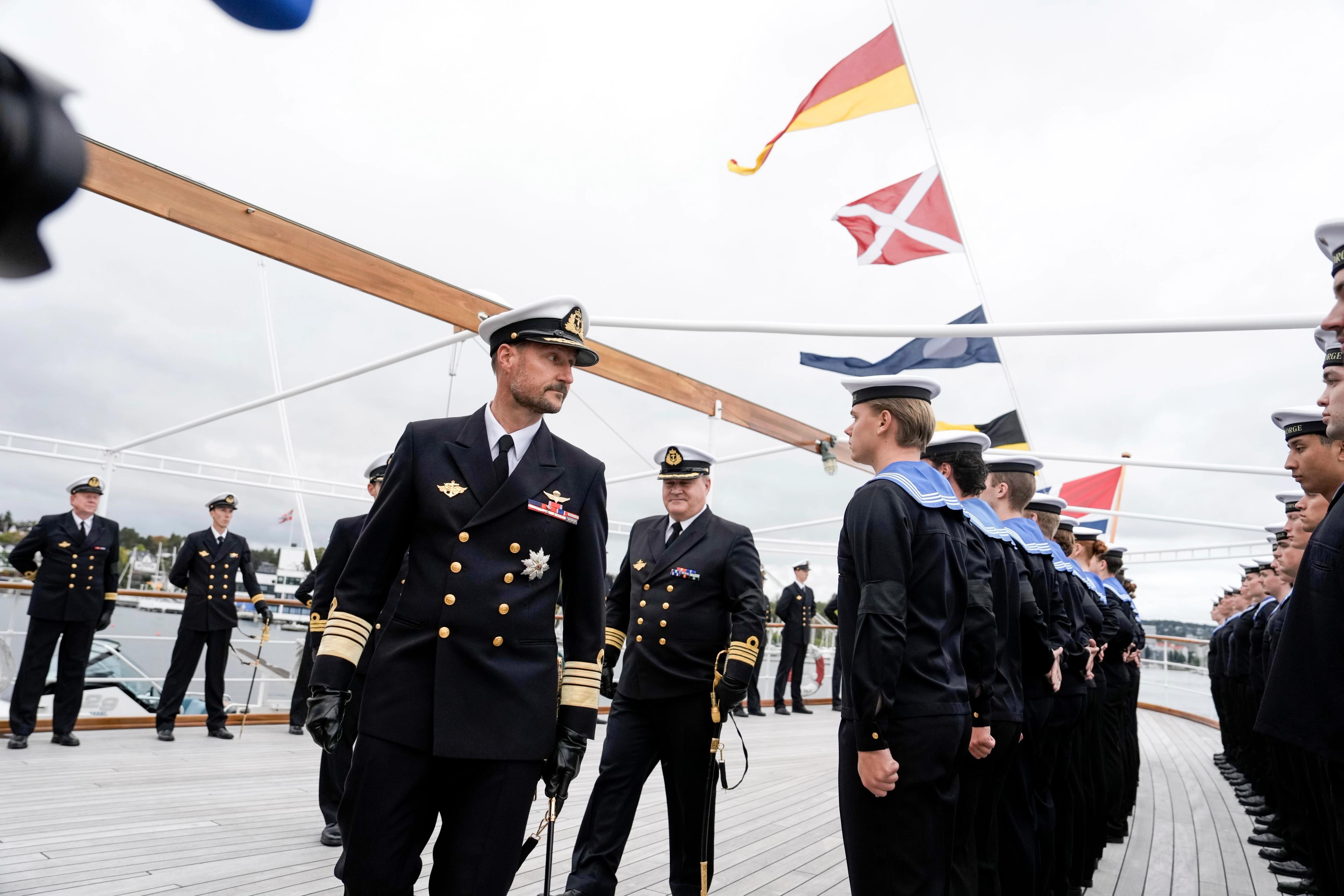 Kong Haakon passerer ei rekkje vernepliktige, medan skipssjefen går bak.