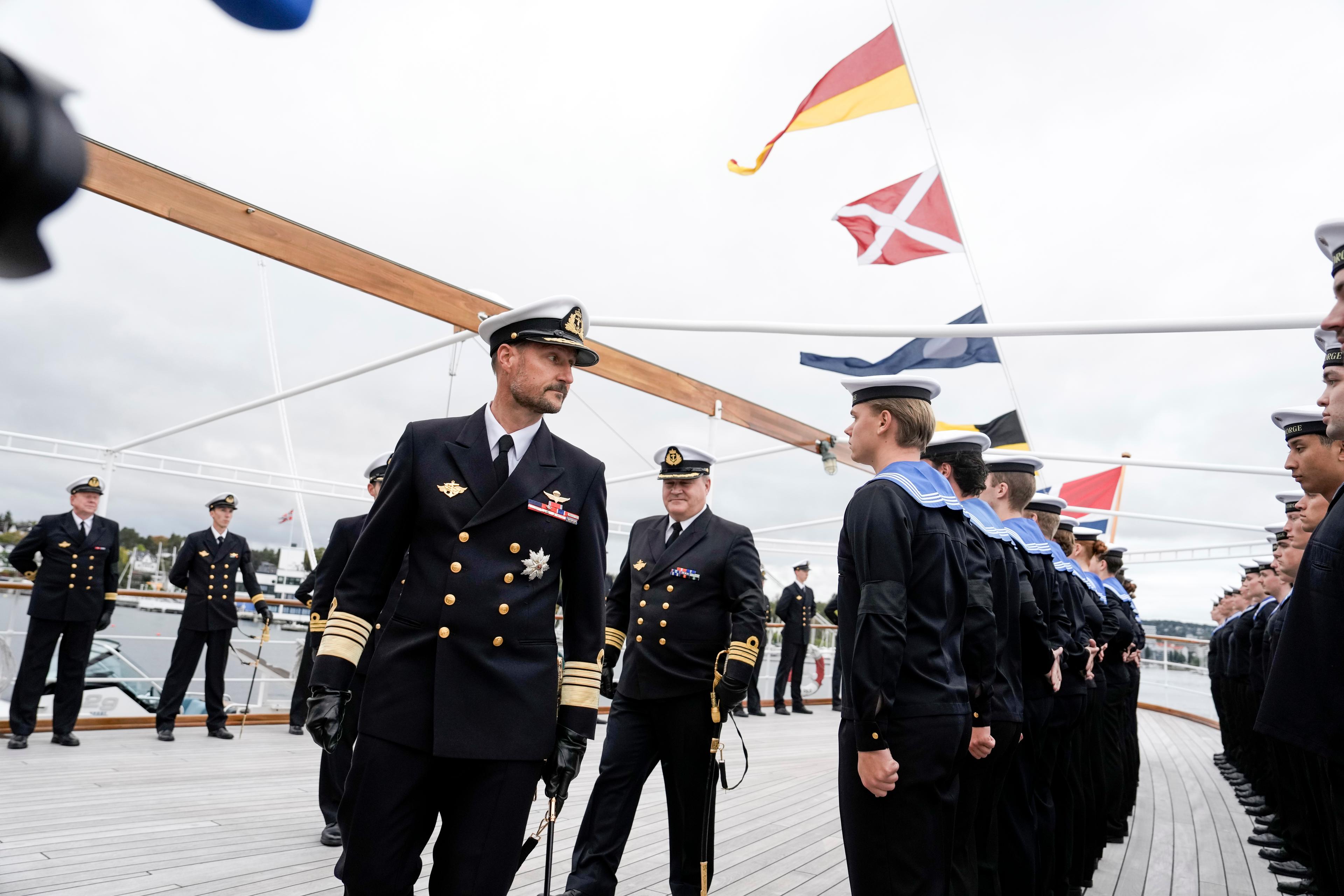 Kong Haakon passerer ei rekkje vernepliktige, medan skipssjefen går bak.