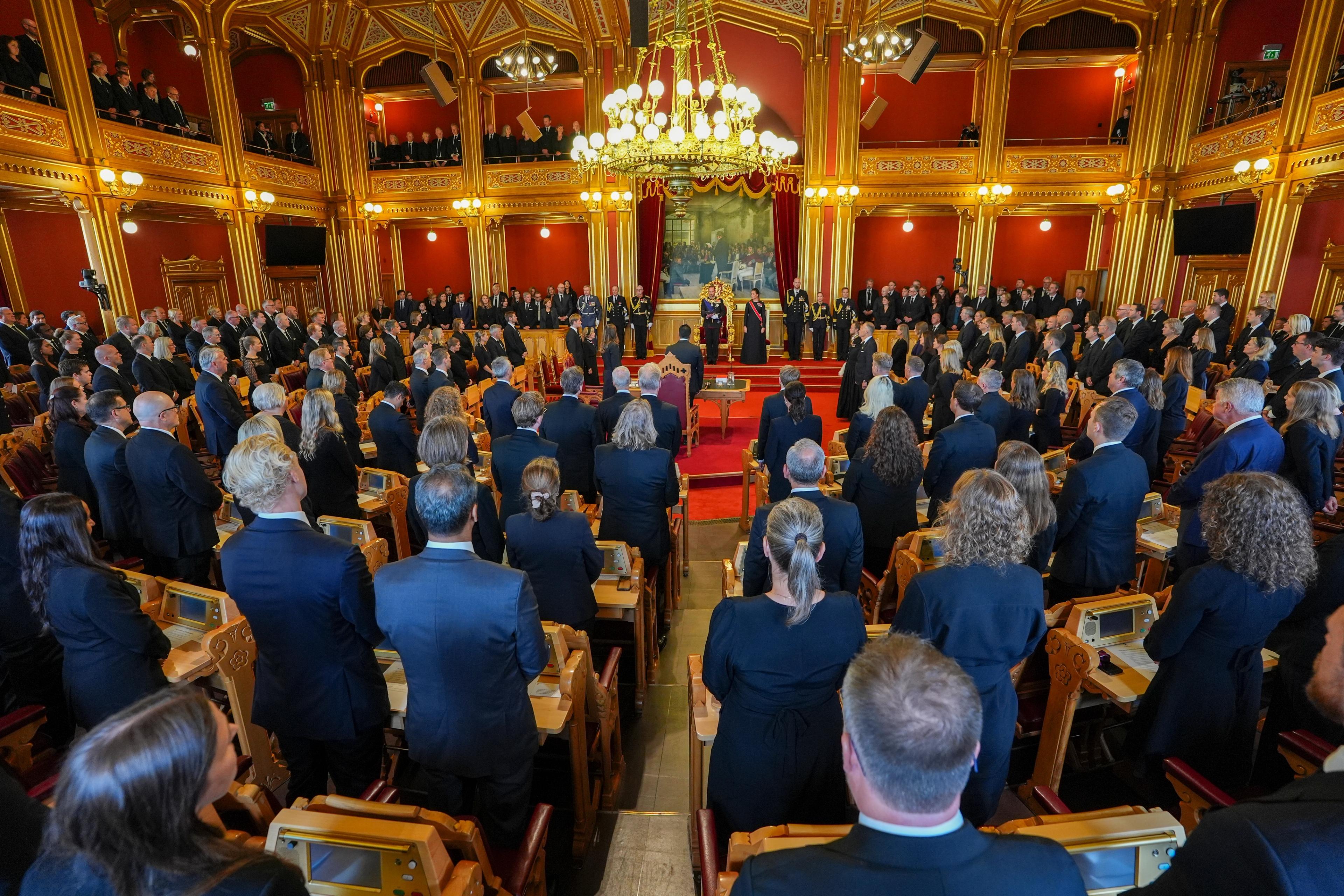 Oversiktsbilde fra Stortingssalen. Alle representantene står ved plassene sine. Lengst framme, under bildet av Eidsvollforsamlingen, står Kong Haakon og Kronprinsessen.