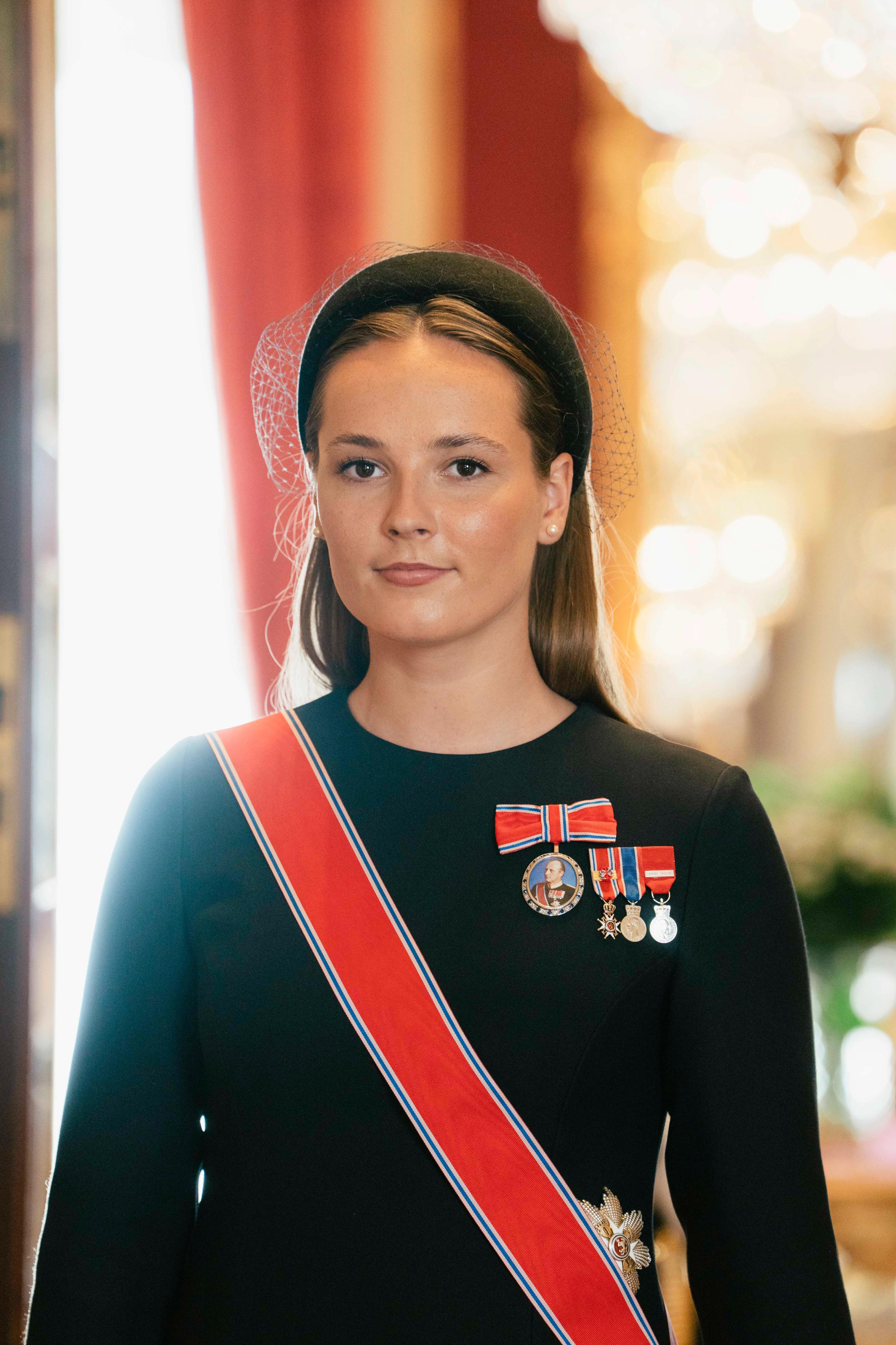 Kronprinsessen i sort kjole. Hun bærer Olavs orden, Kong Haralds portrettnål og miniatyrer av tre andre medaljer.