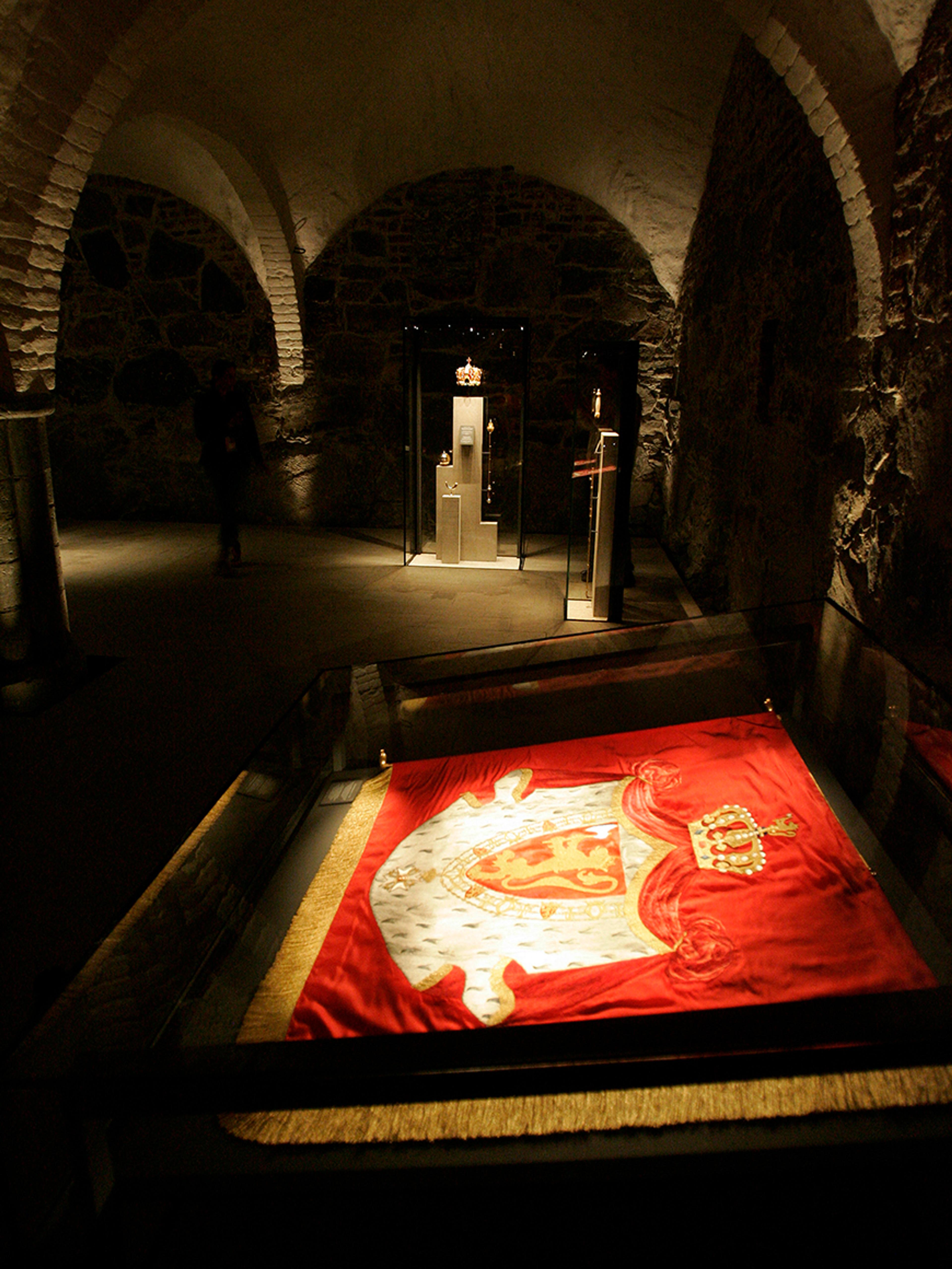 Det røde banneret ligger i monter. Bakom skimtes kongekronen.