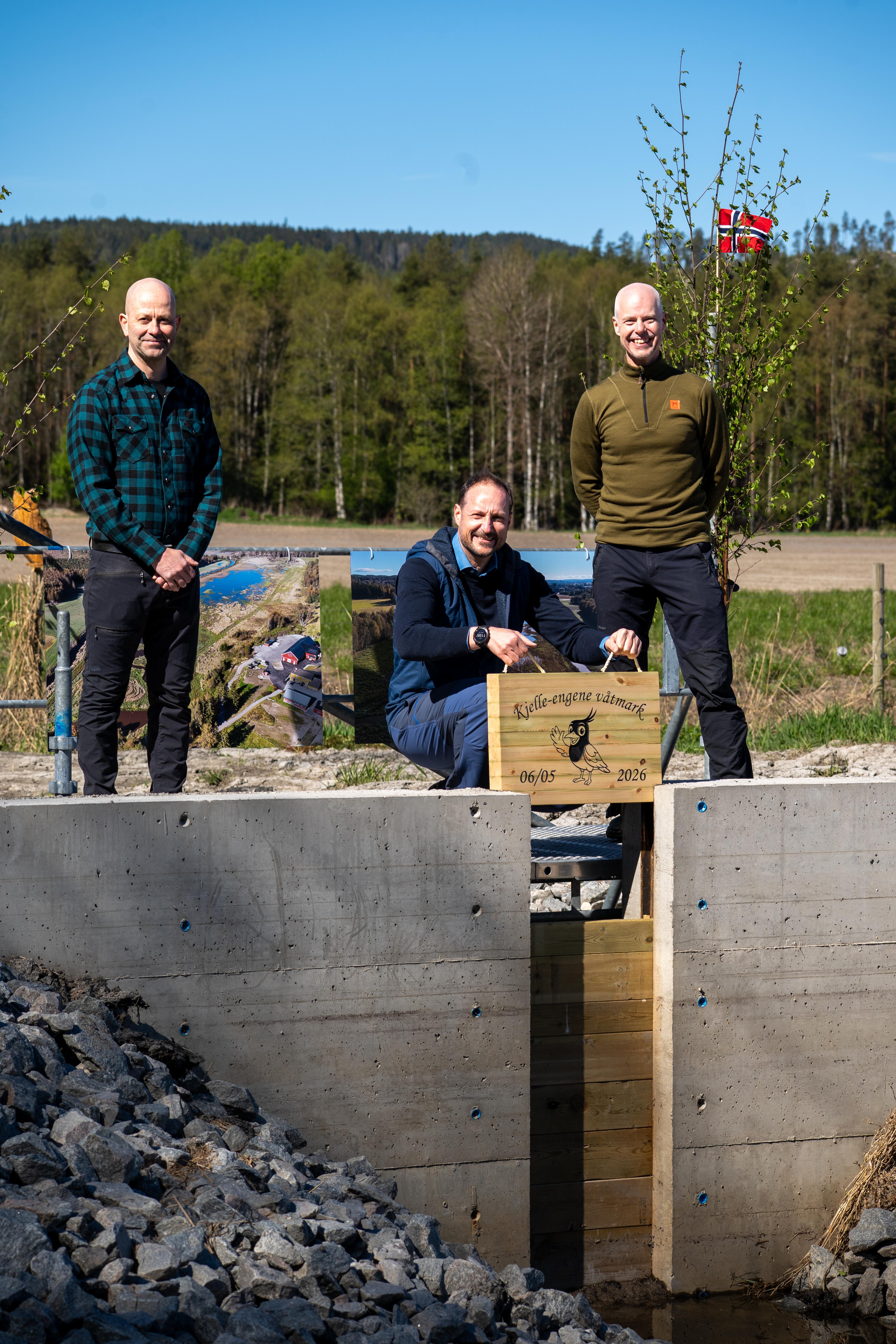 Kronprins Haakon på huk med planken i hendene, med våtmarkskameratene smilende på hver side.