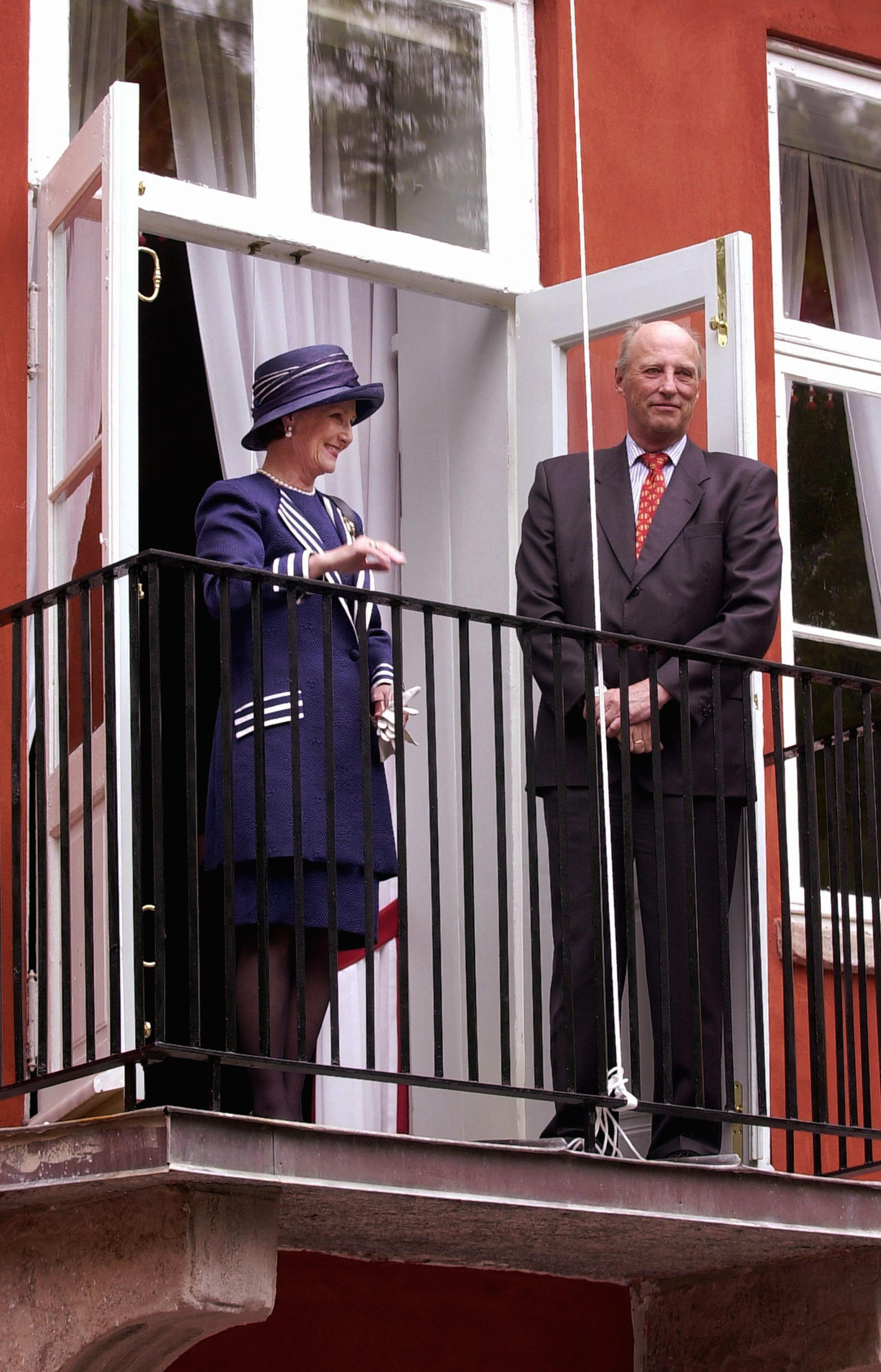 Kongeparet står smilende på balkongen.