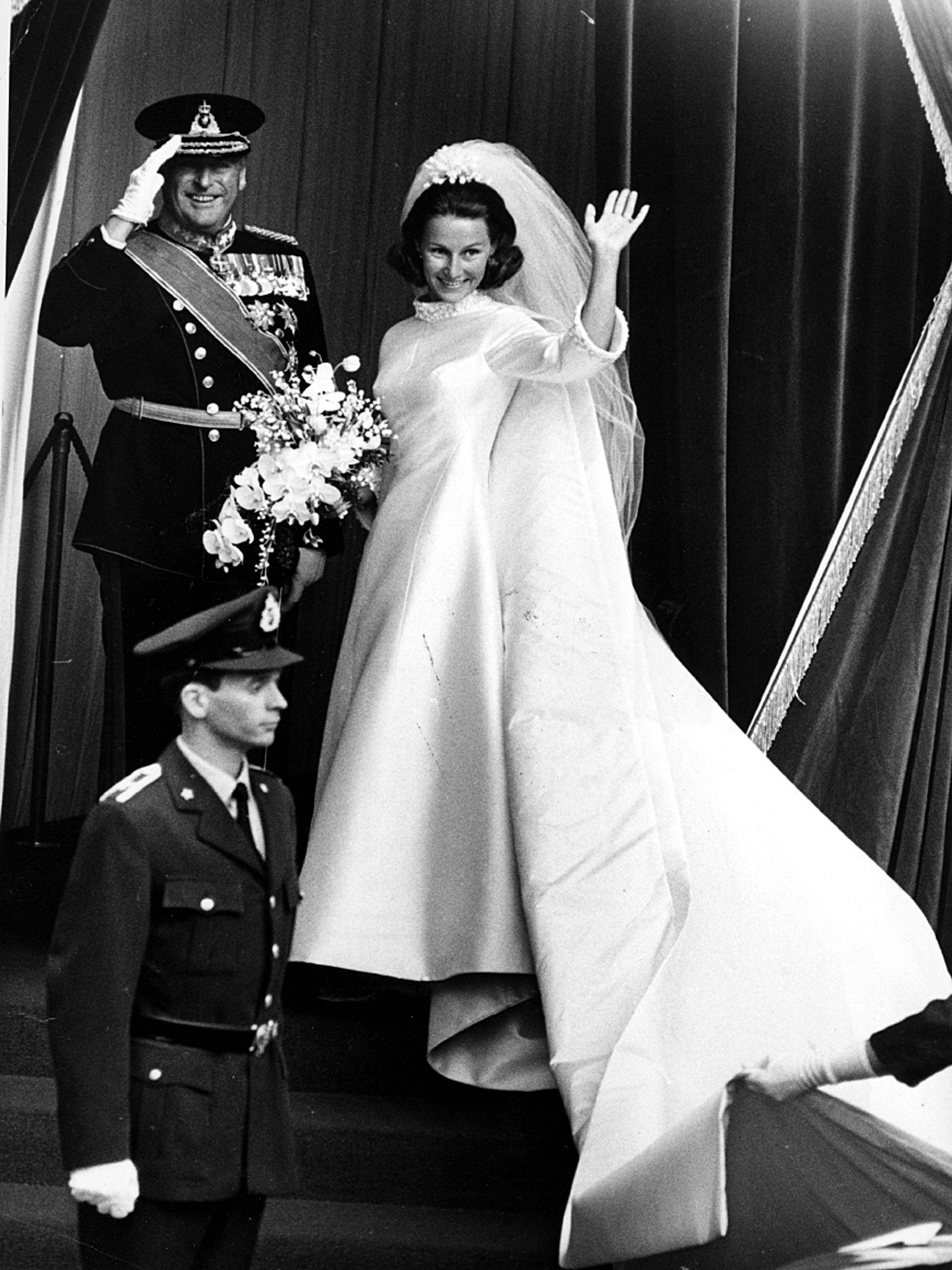 Den kommende kronprinsessen på vei inn i kirken snur seg og vinker. En smilende Kong Olav i gallauniform gjør honnør som hilsen til de frammøtte.