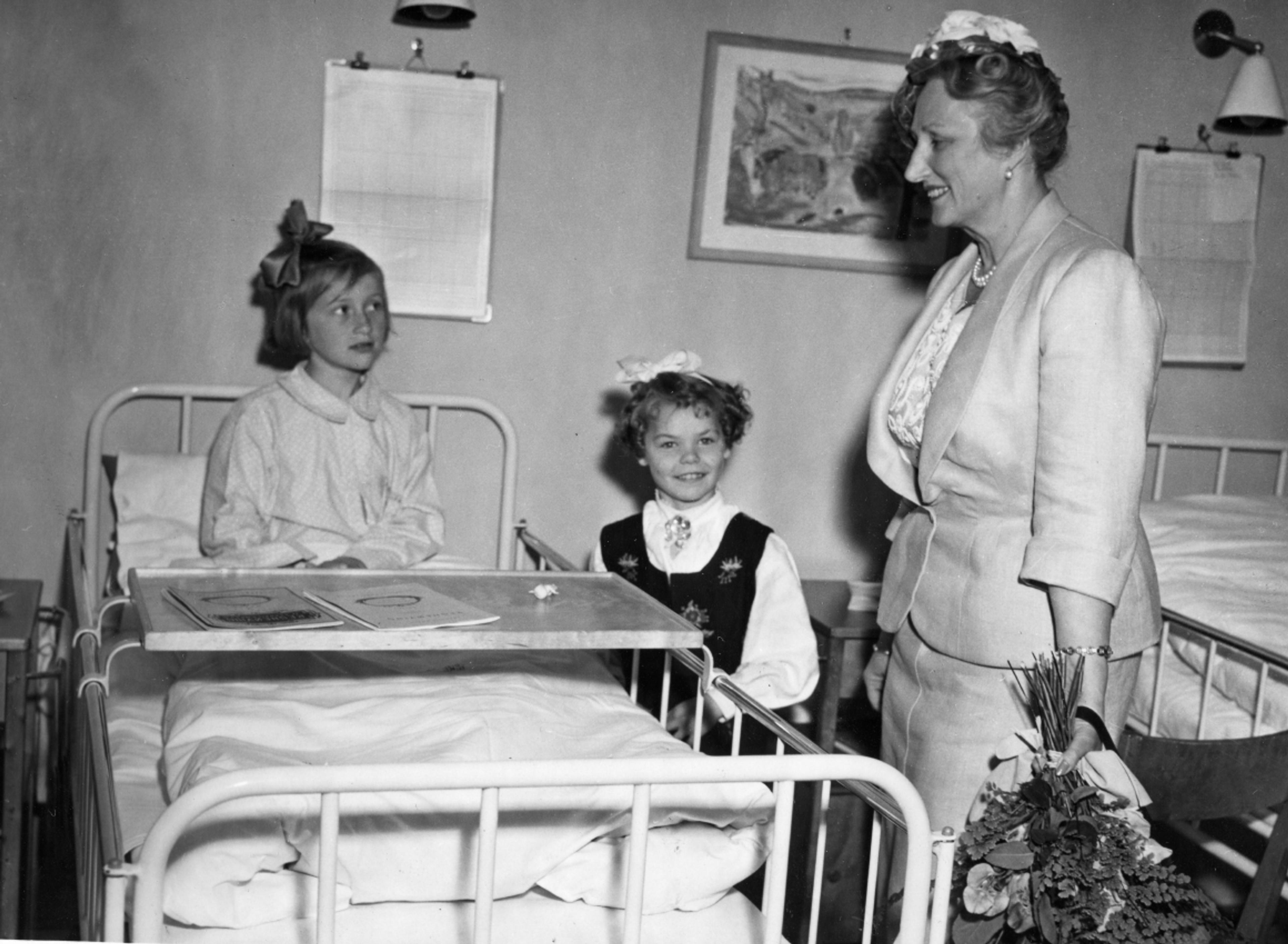 Kronprinsessen står ved siden av en sykeseng med en liten pike i.