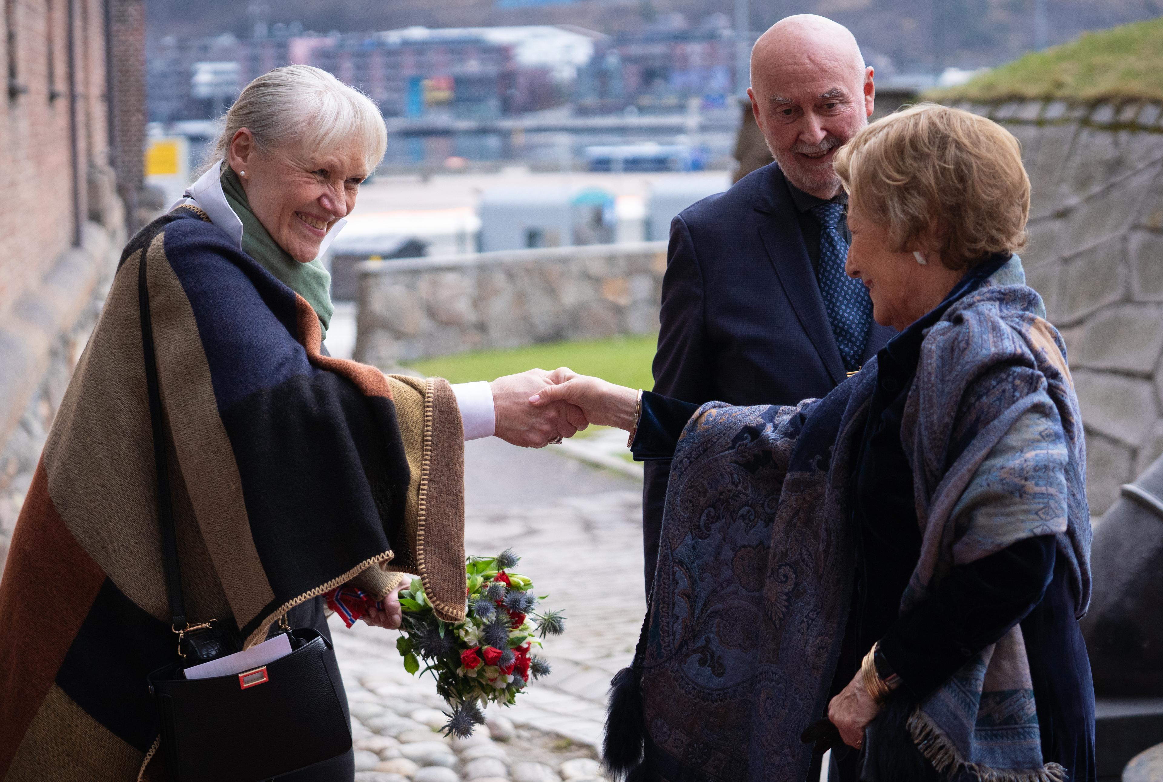 Dagleg leiar helsar på Dronning Sonja utandørs på Akershus festning. Styreleiar står i bakgrunnen.