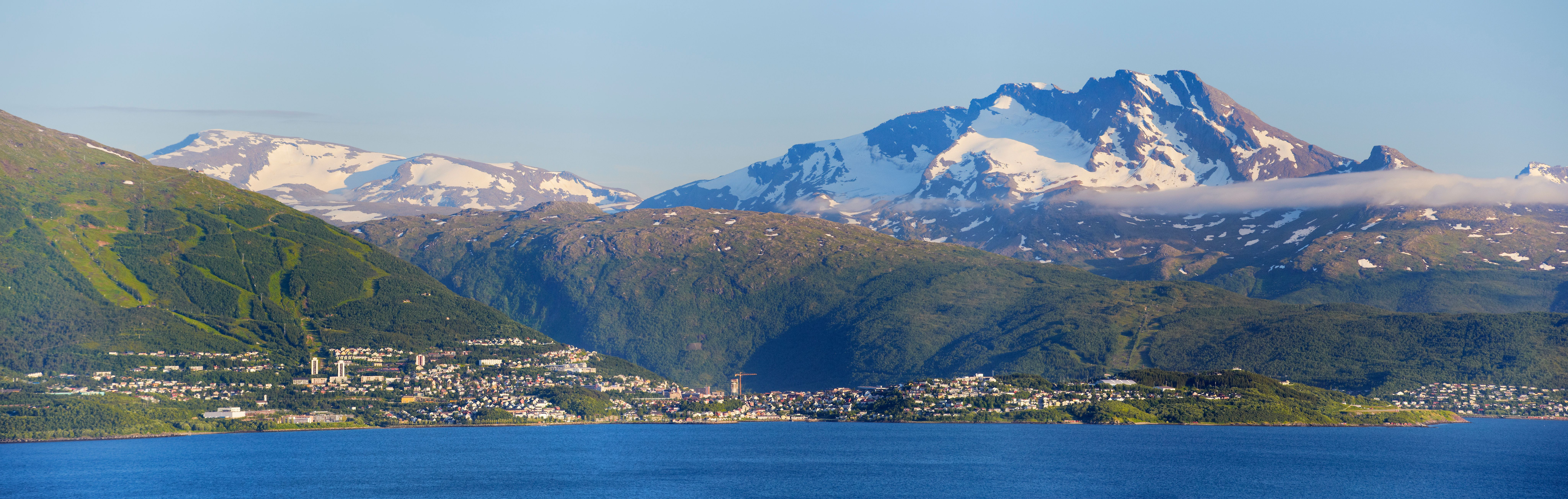 Oversiktsbilde tatt fra sjøsiden. Narvik by med fjellene bak. De høyeste er snødekte.