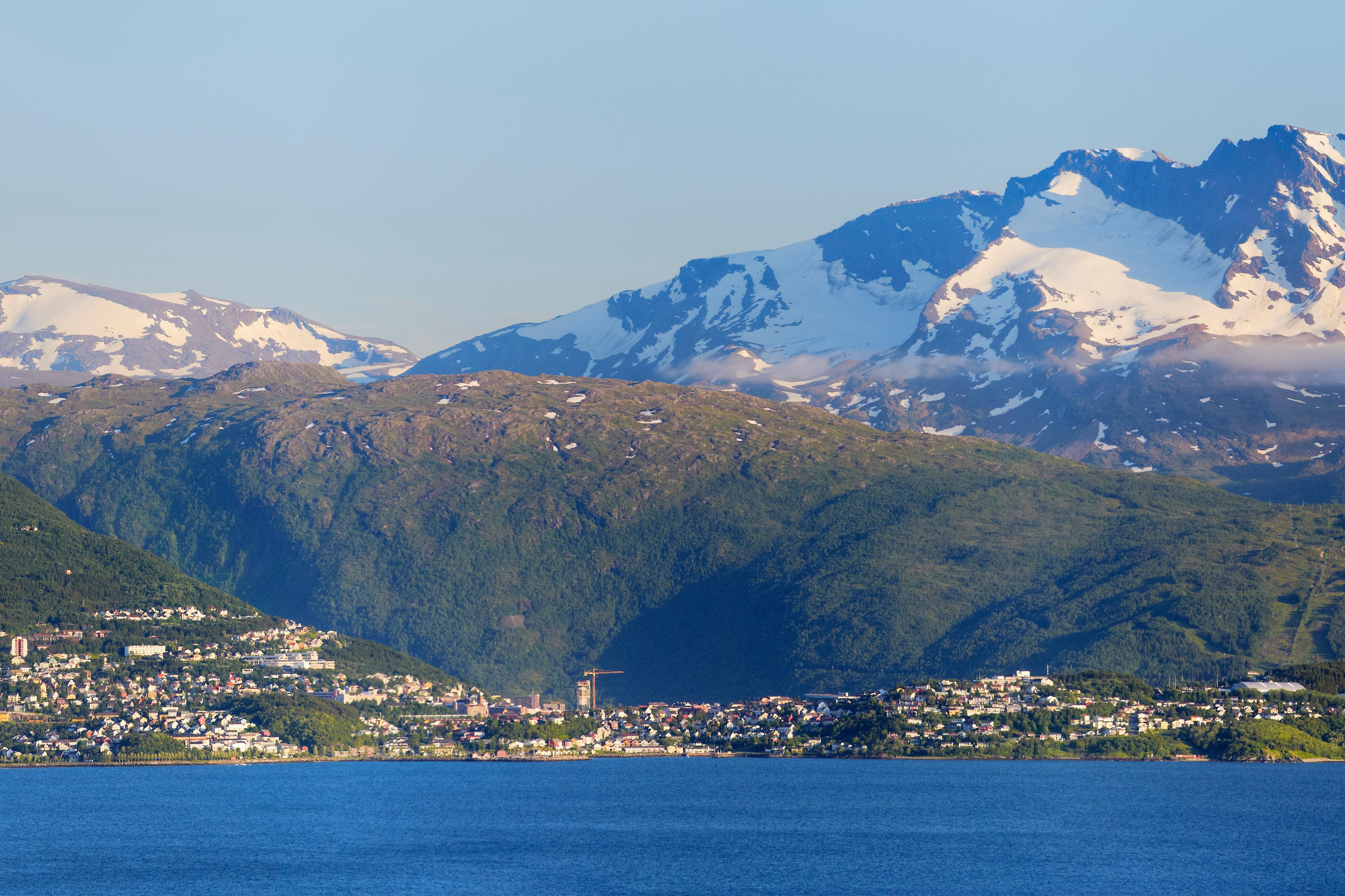 Oversiktsbilde tatt fra sjøsiden. Narvik by med fjellene bak. De høyeste er snødekte.