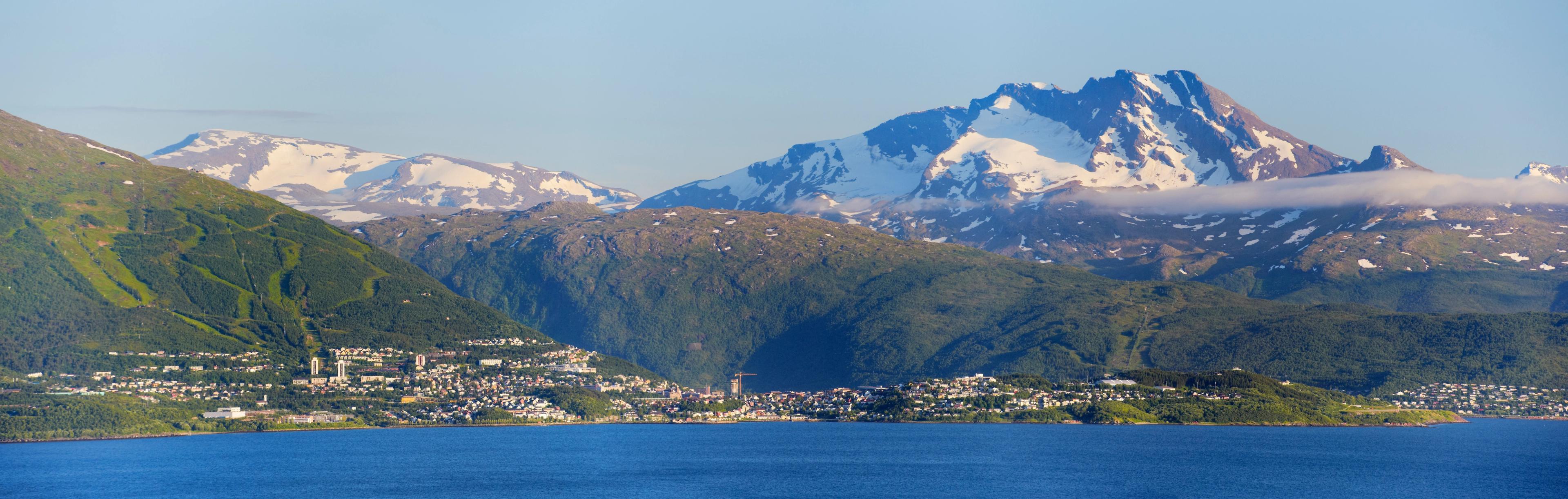 Oversiktsbilde tatt fra sjøsiden. Narvik by med fjellene bak. De høyeste er snødekte.