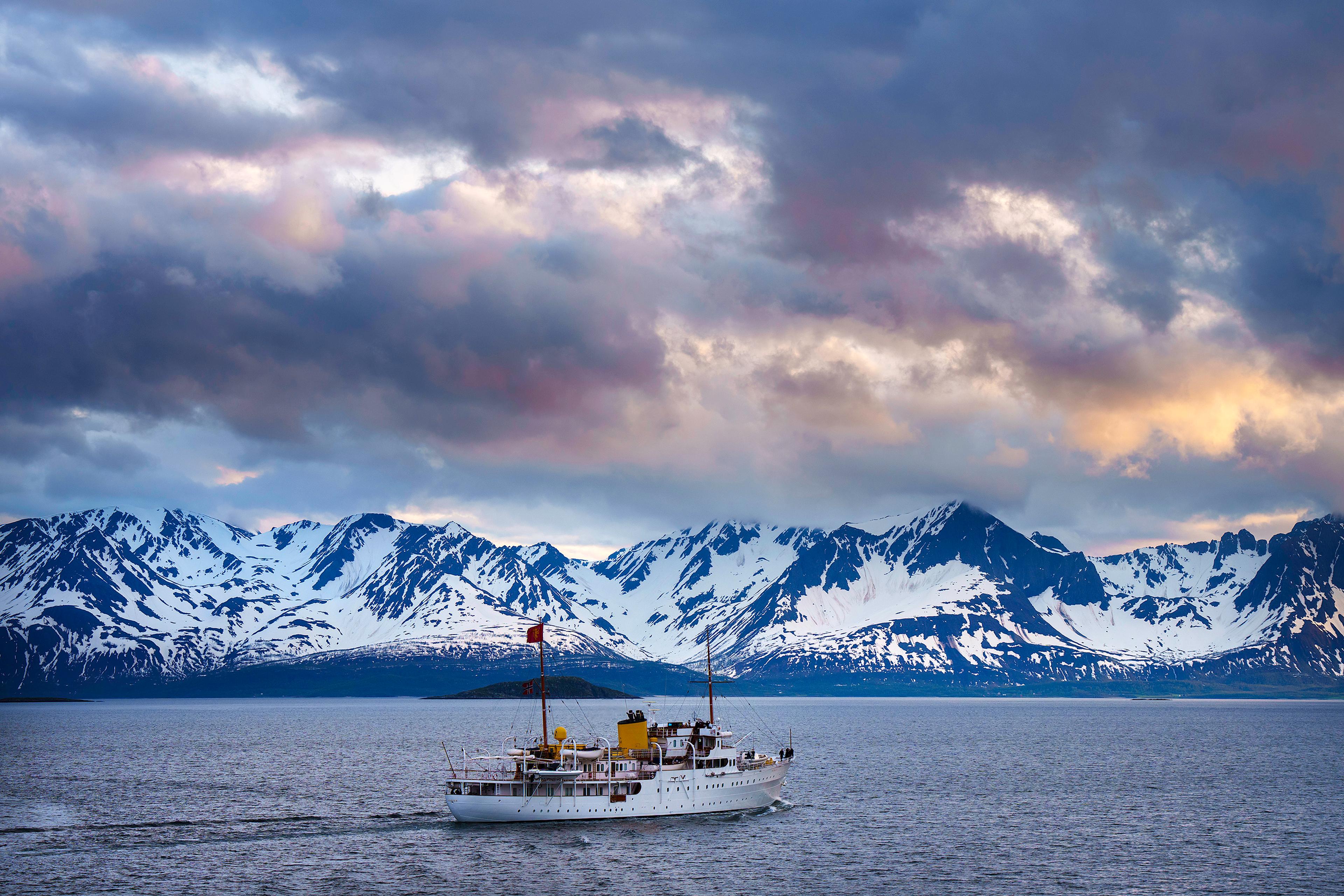 Kongeskipet med skyer i solnedgang og snødekte fjell i bakgrunnen.