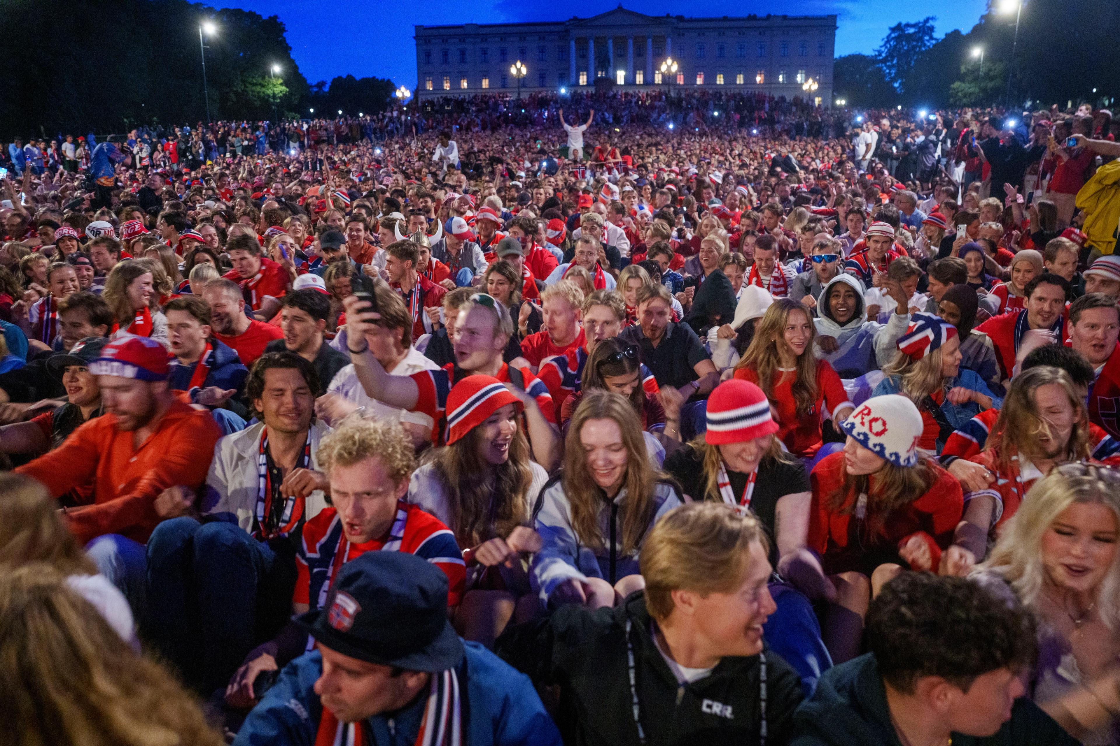Tusenvis av mennesker sitter på bakken foran Slottet og ror.