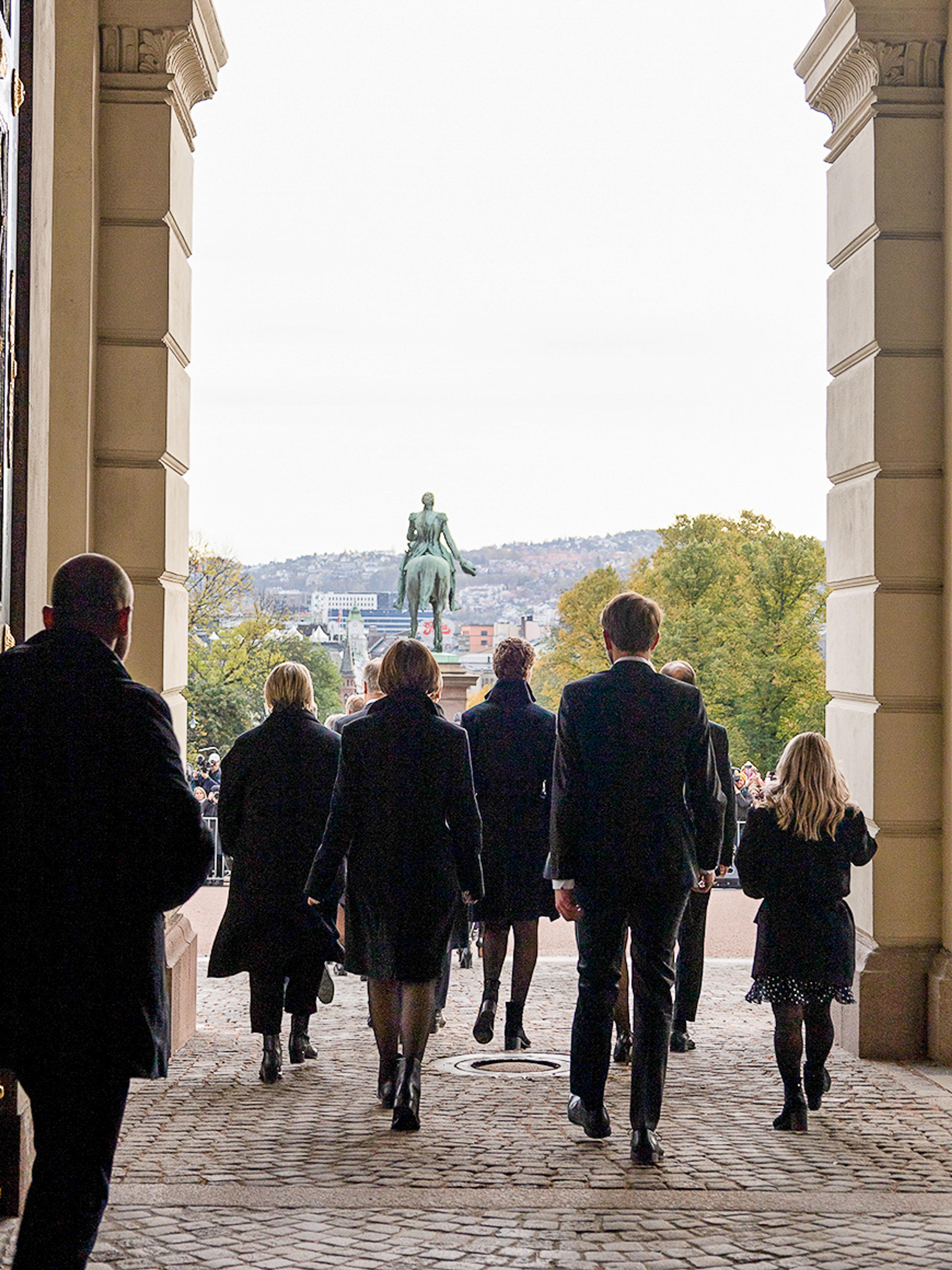 Vi ser regjeringen bakfra idet de passerer ut gjennom Slottets hovedport og ut på Slottsplassen.