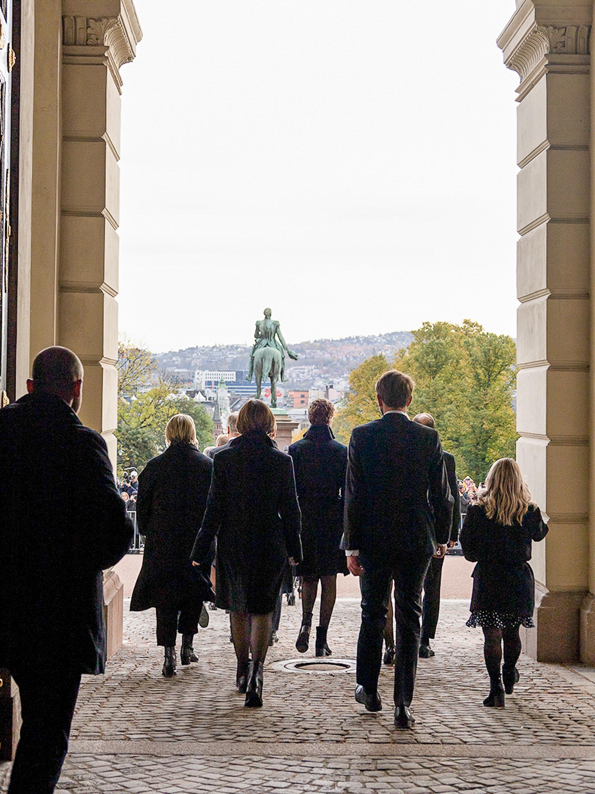 Vi ser regjeringen bakfra idet de passerer ut gjennom Slottets hovedport og ut på Slottsplassen.