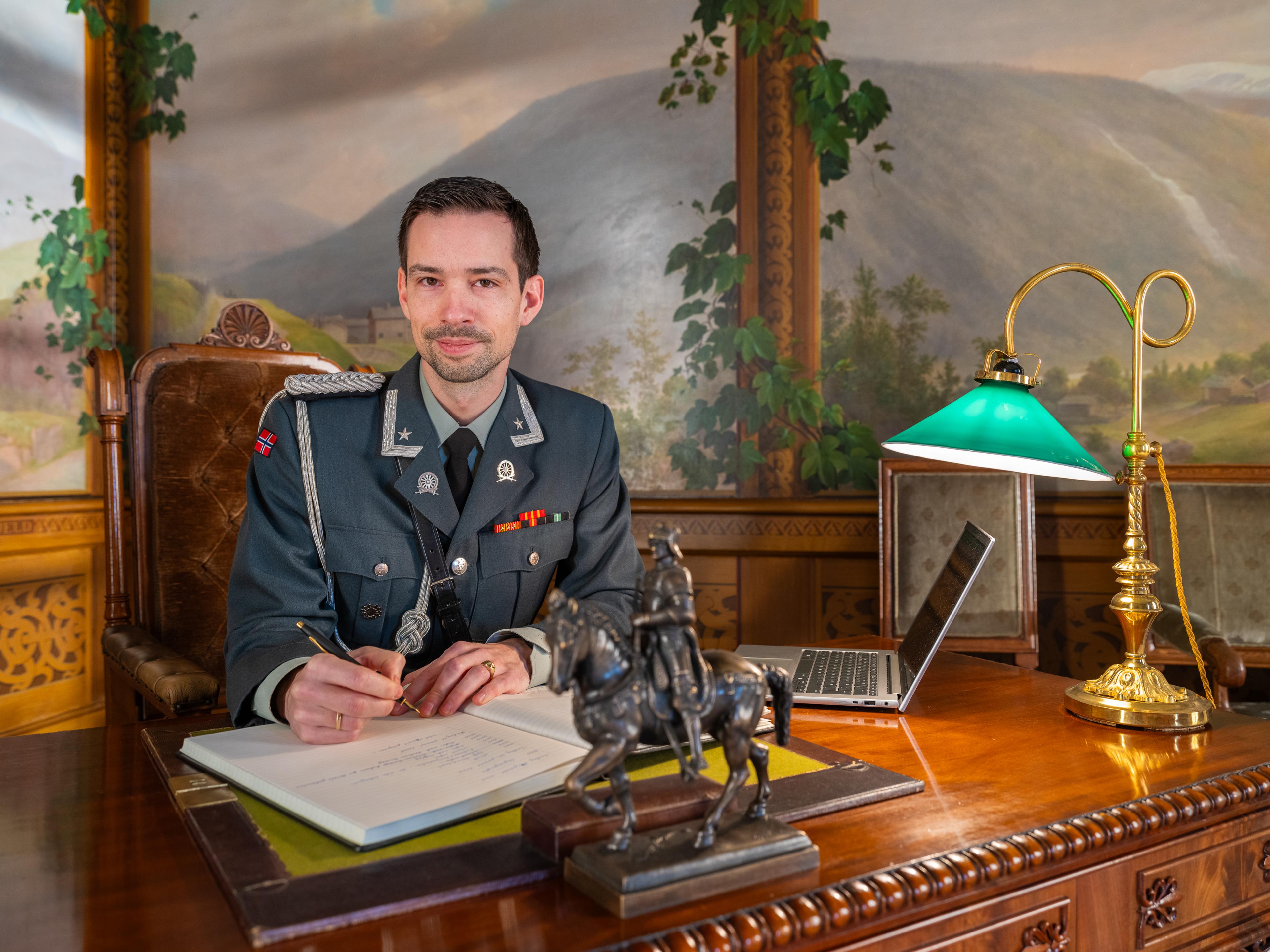 Adjutant sitter ved et stort skrivebord og fører tekst inn i en stor protokollbok.