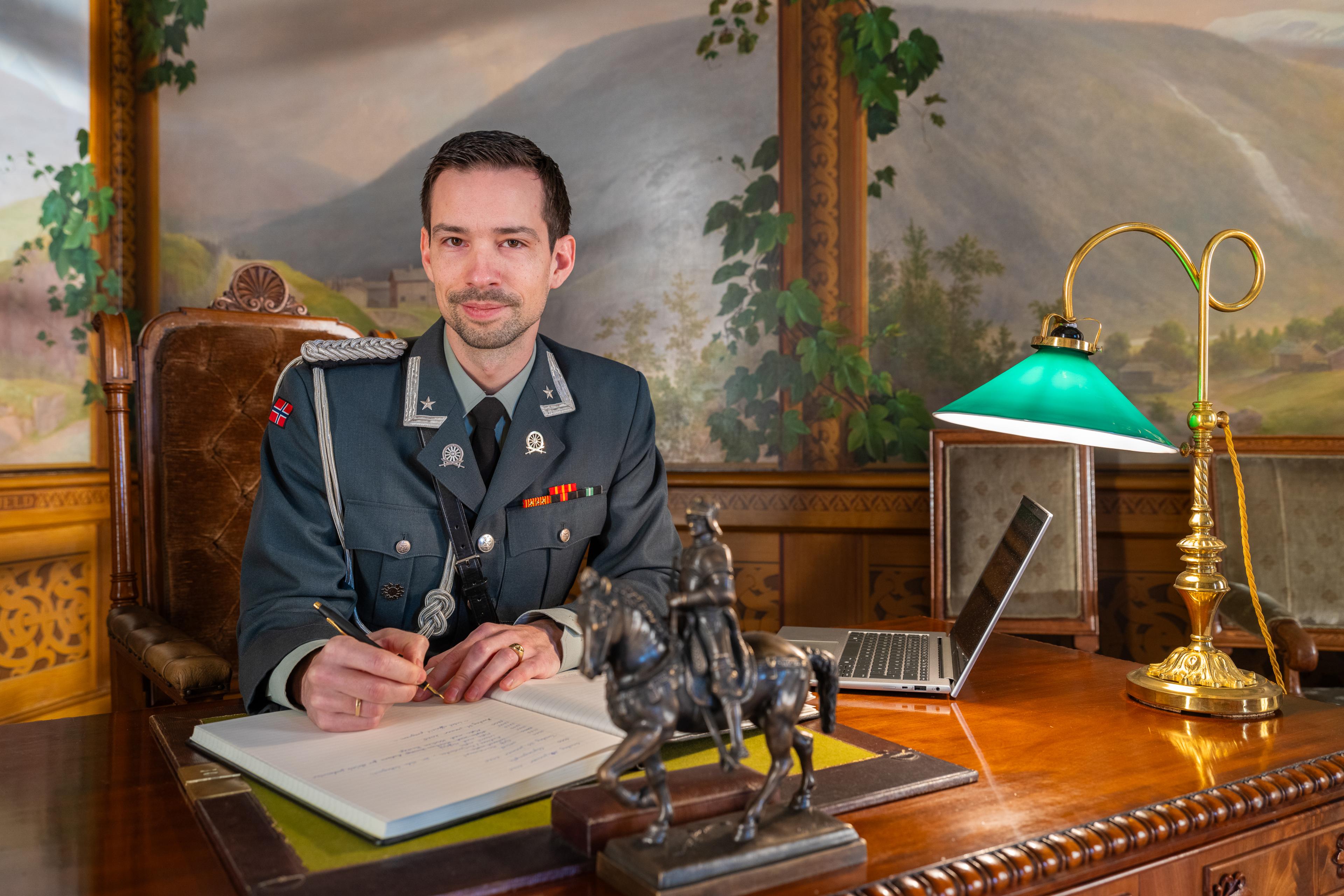 Adjutant sitter ved et stort skrivebord og fører tekst inn i en stor protokollbok.