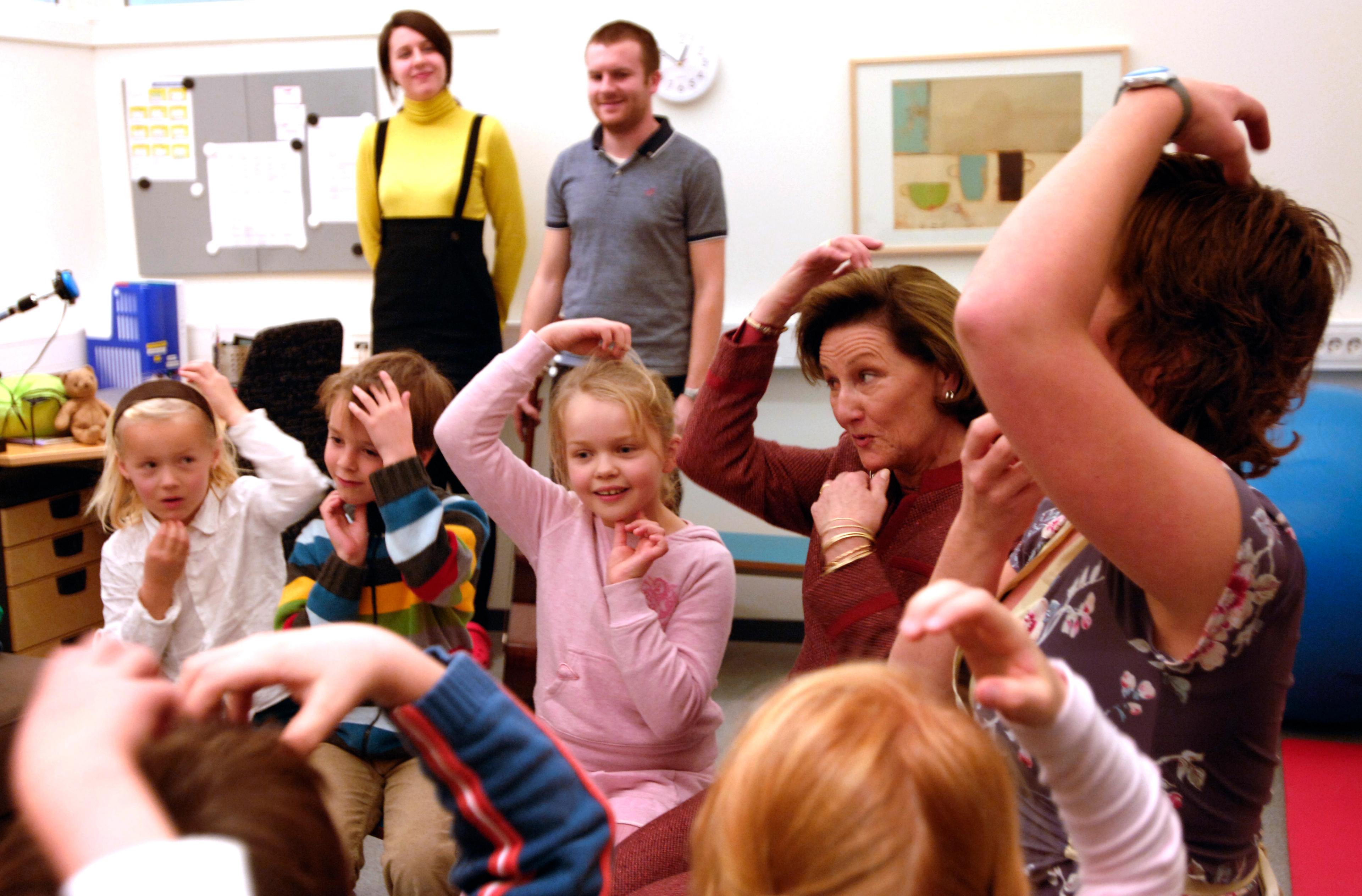 Dronning Sonja og barneskoleelever gjør bevegelser til sang.